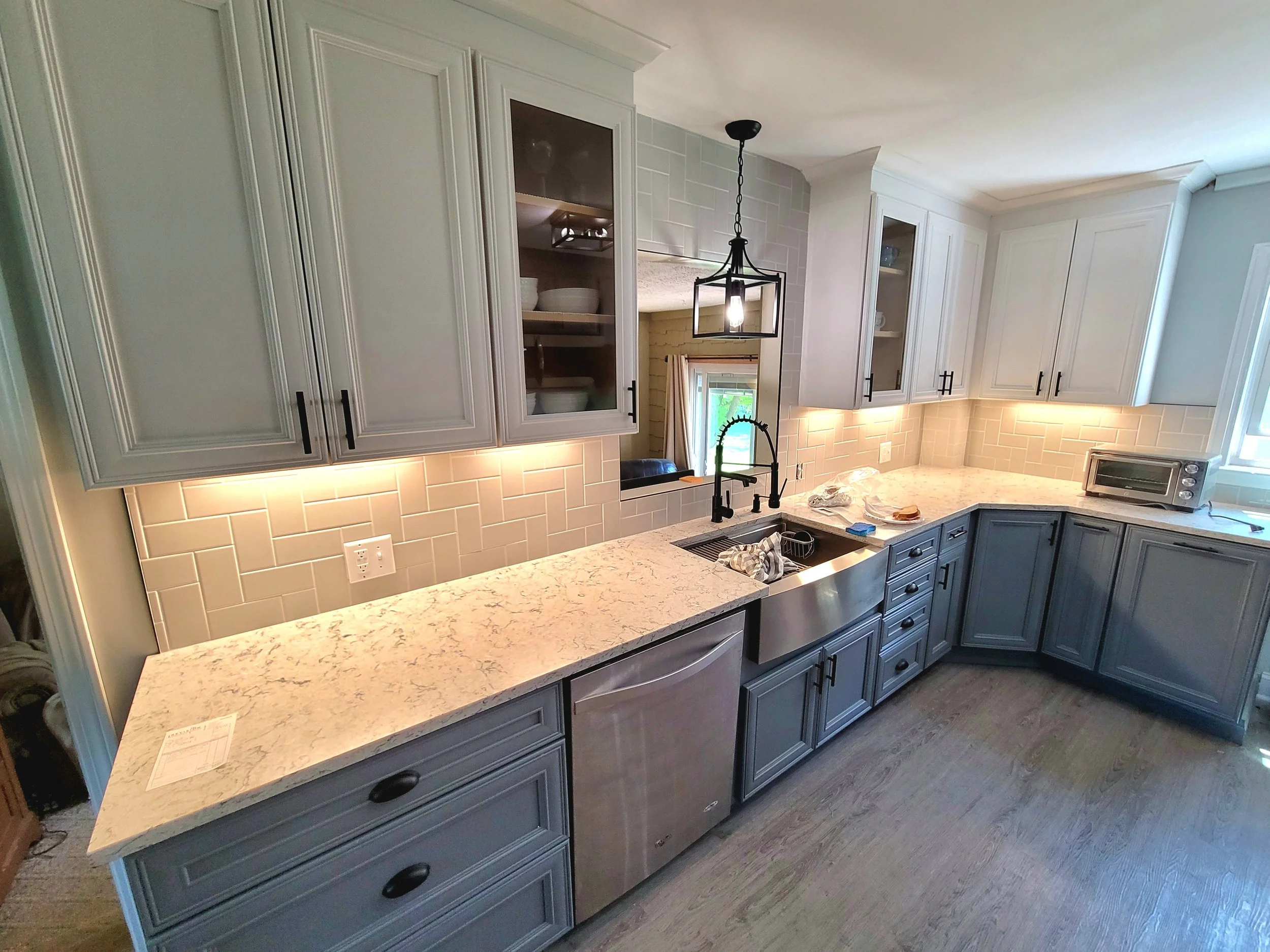 A modern kitchen with blue cabinets, white marble countertops, a beige tile backsplash, and a black chandelier hanging from the ceiling.