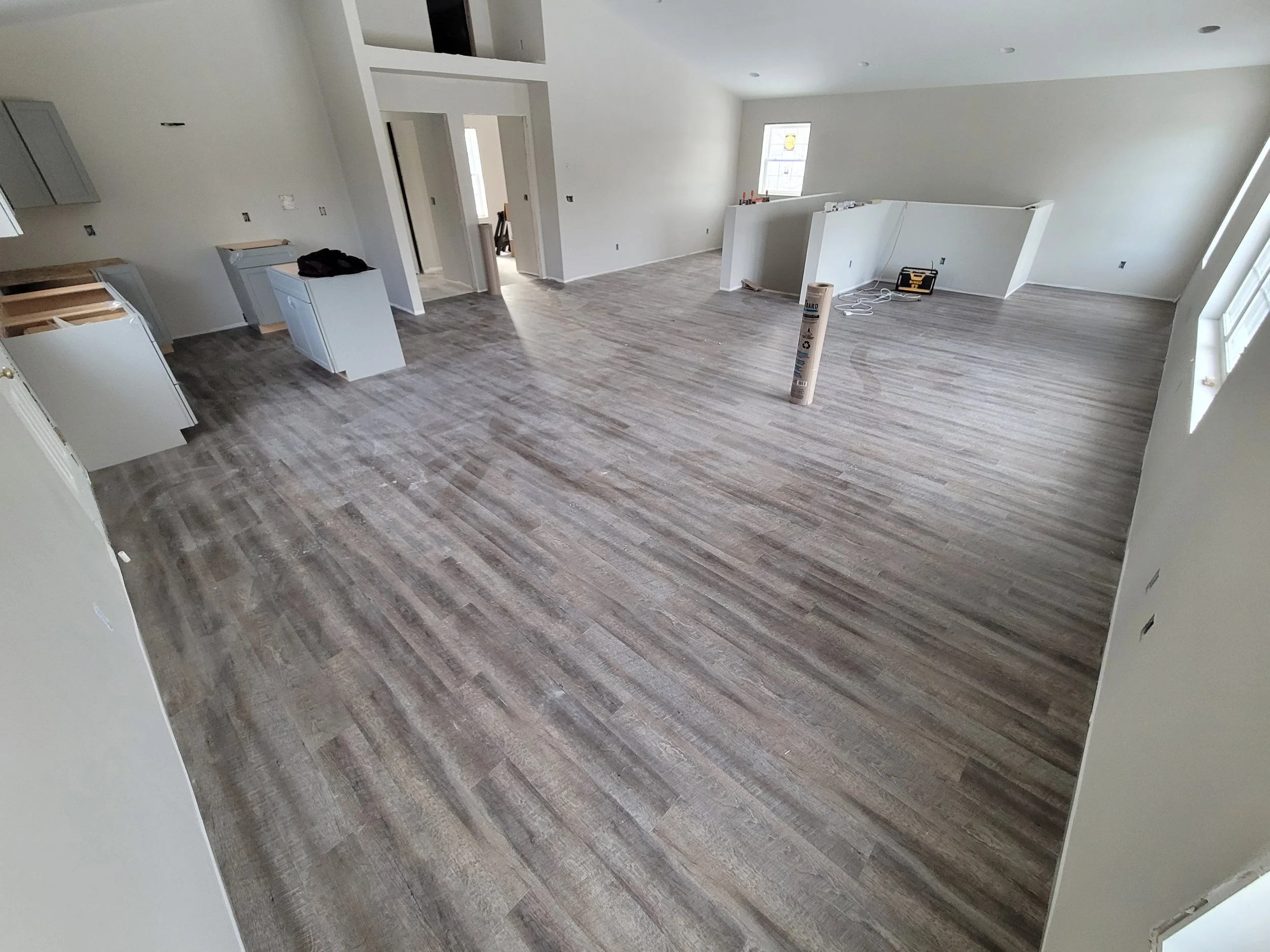 Empty room with light-colored wood flooring, white walls, and windows, with some construction or renovation materials and tools present.