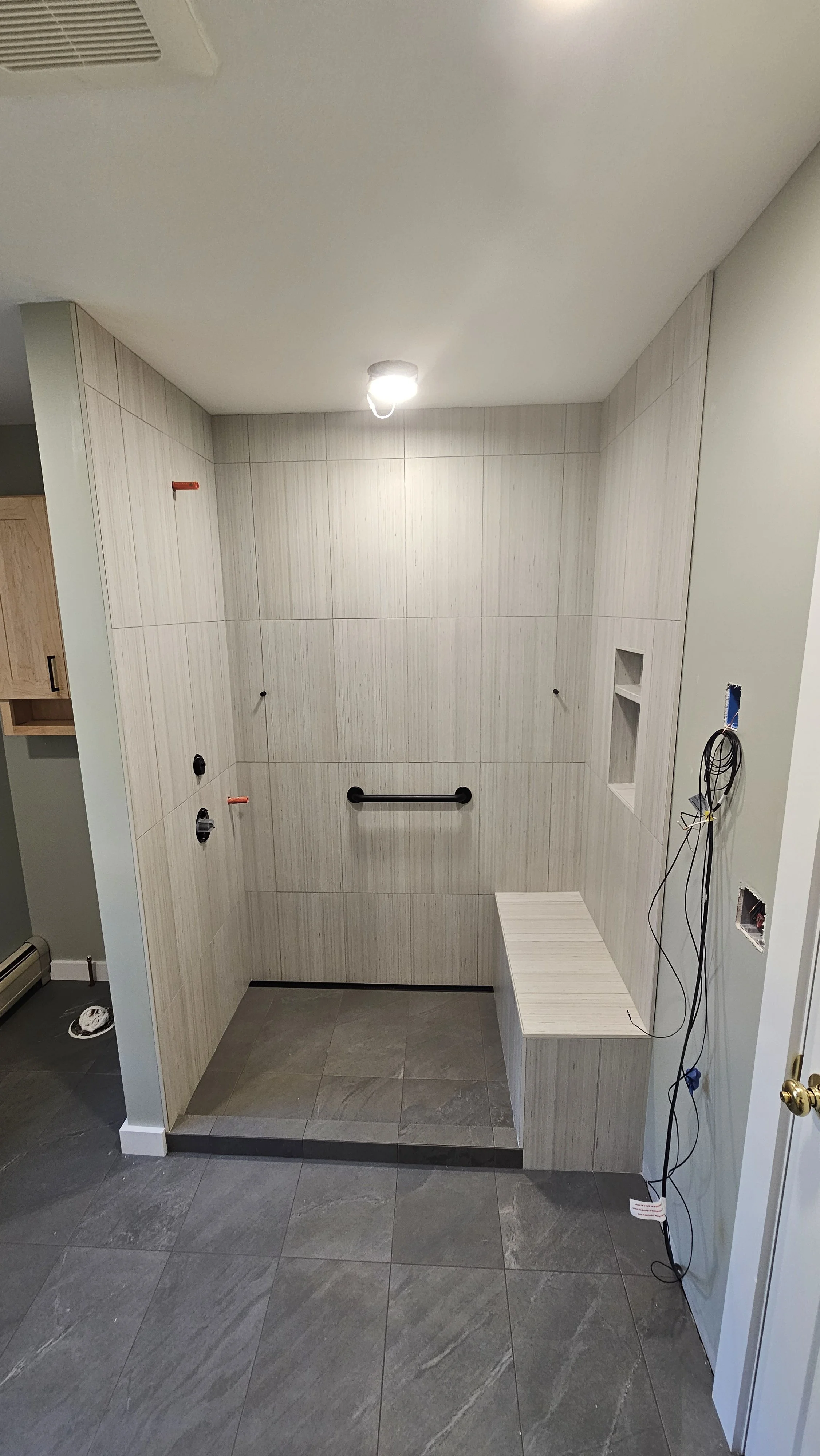 Bathroom or shower area under construction with tiled walls, a bench, and exposed electrical wiring.