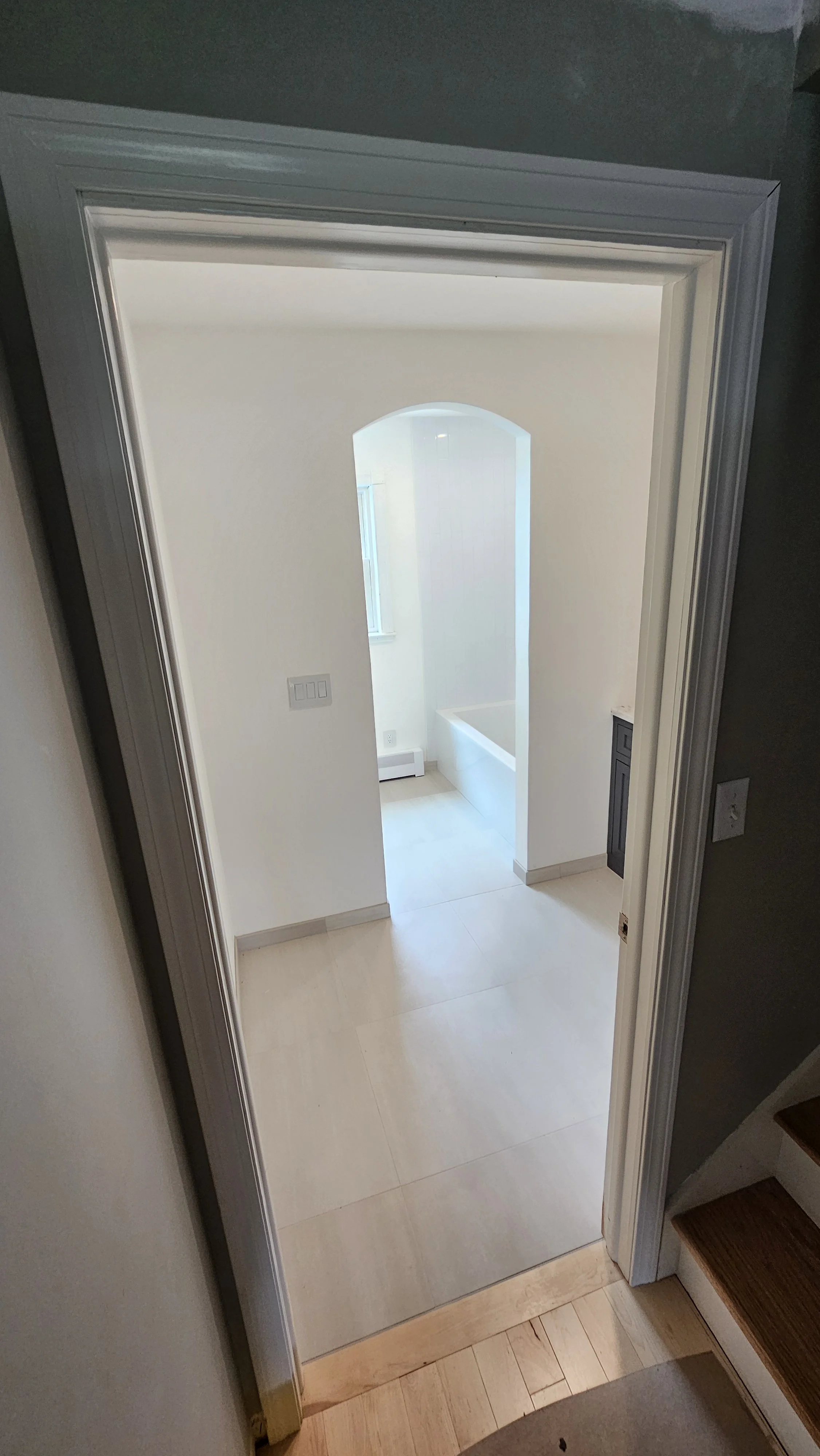 View through an open door into a bathroom with a bathtub, a window, and a white wall.