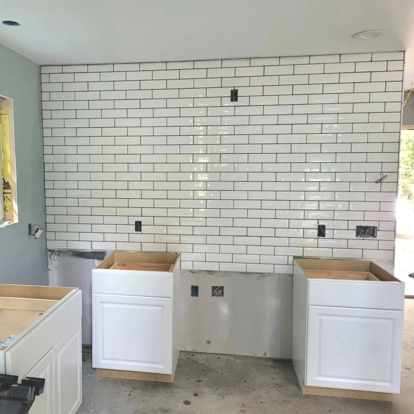 Kitchen renovation in progress with white cabinets and a white subway tile backsplash wall.