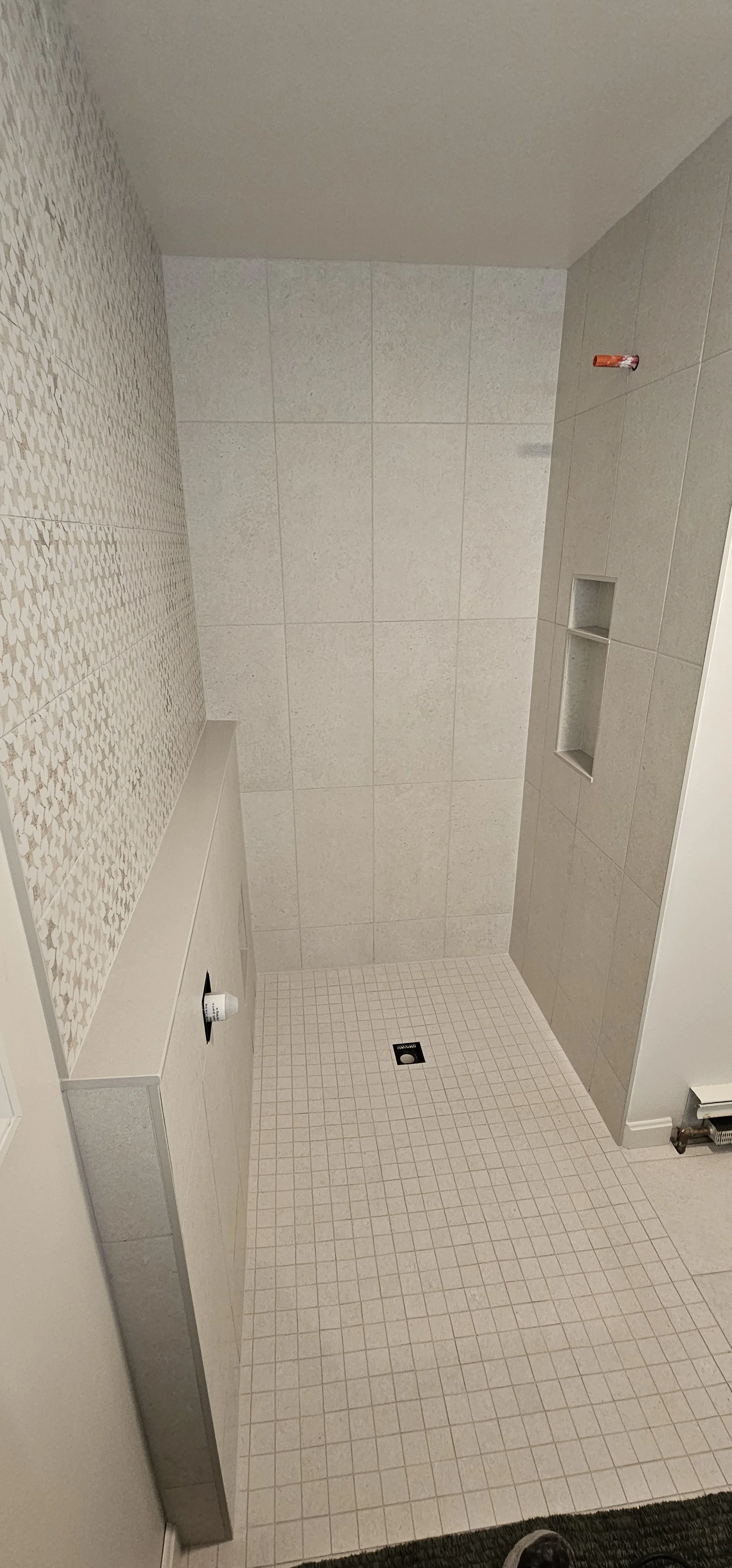 Bare bathroom shower with wall tiles, built-in shelf, and a drain in the floor. No showerhead or fixtures visible.