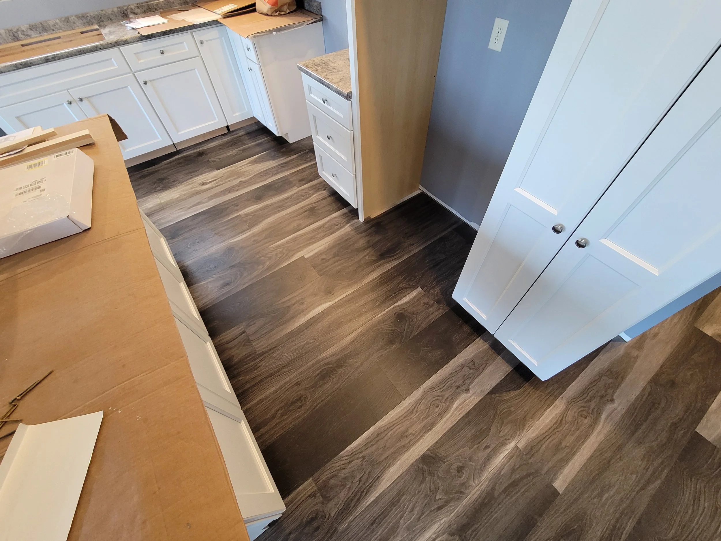 A kitchen with white cabinets, a granite countertop, and dark wood-look flooring. There is a white cabinet with drawers and a blue wall.
