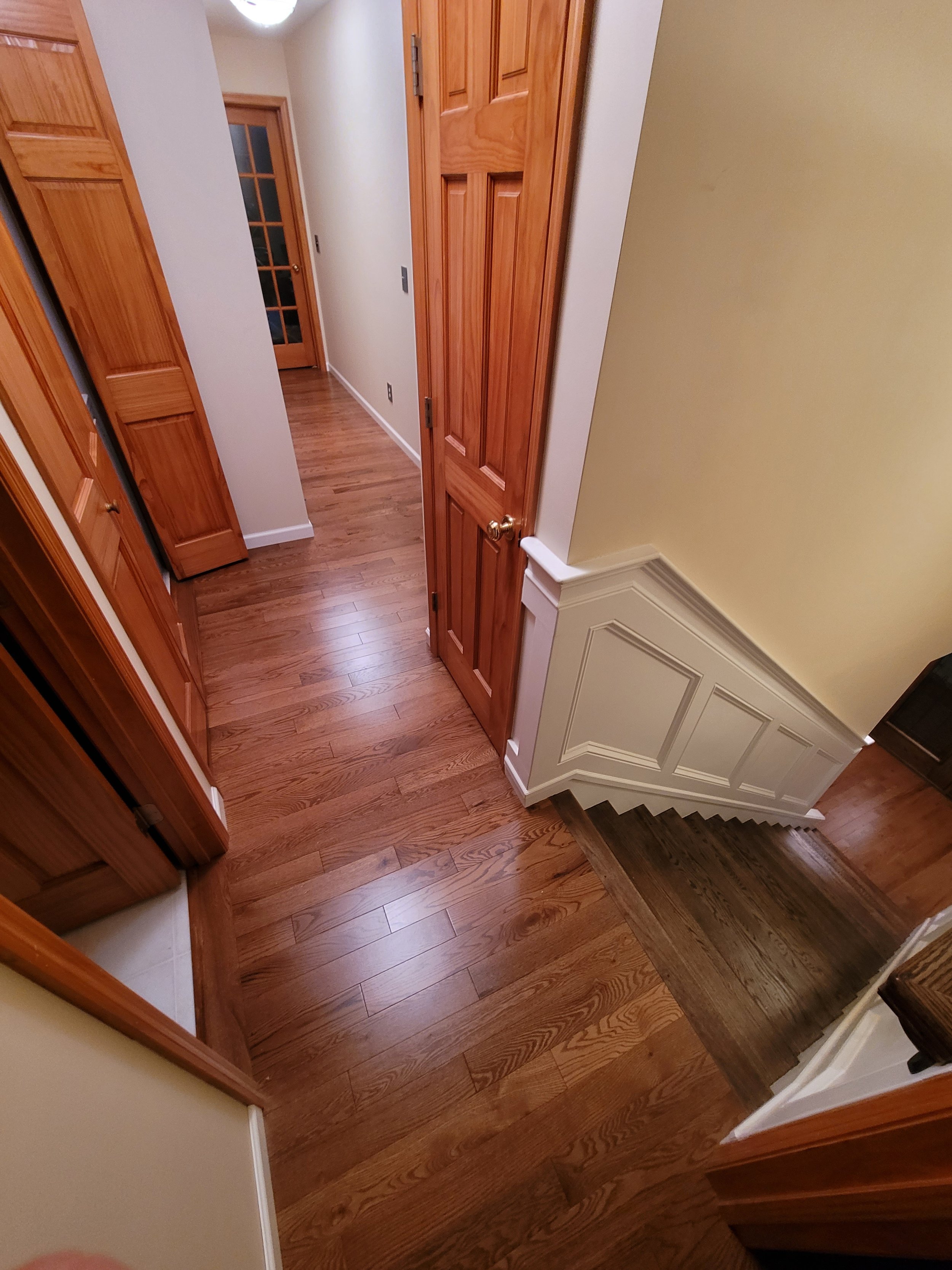 A hallway with wooden flooring and wooden doors, including a door with glass panes, and paneled walls.