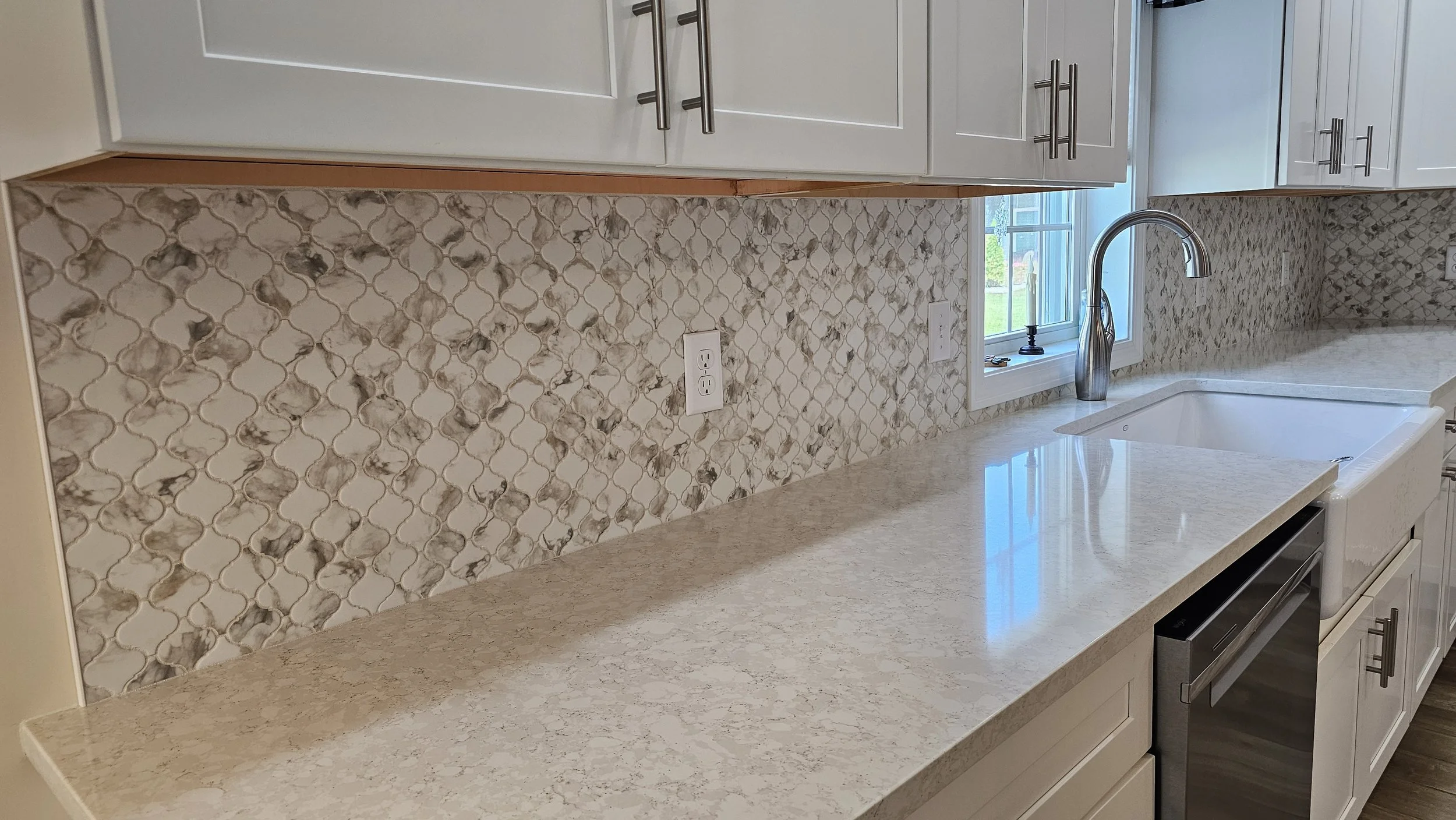 Kitchen with white cabinets, a speckled beige countertop, a patterned tile backsplash, a window above the sink, and a stainless steel faucet.