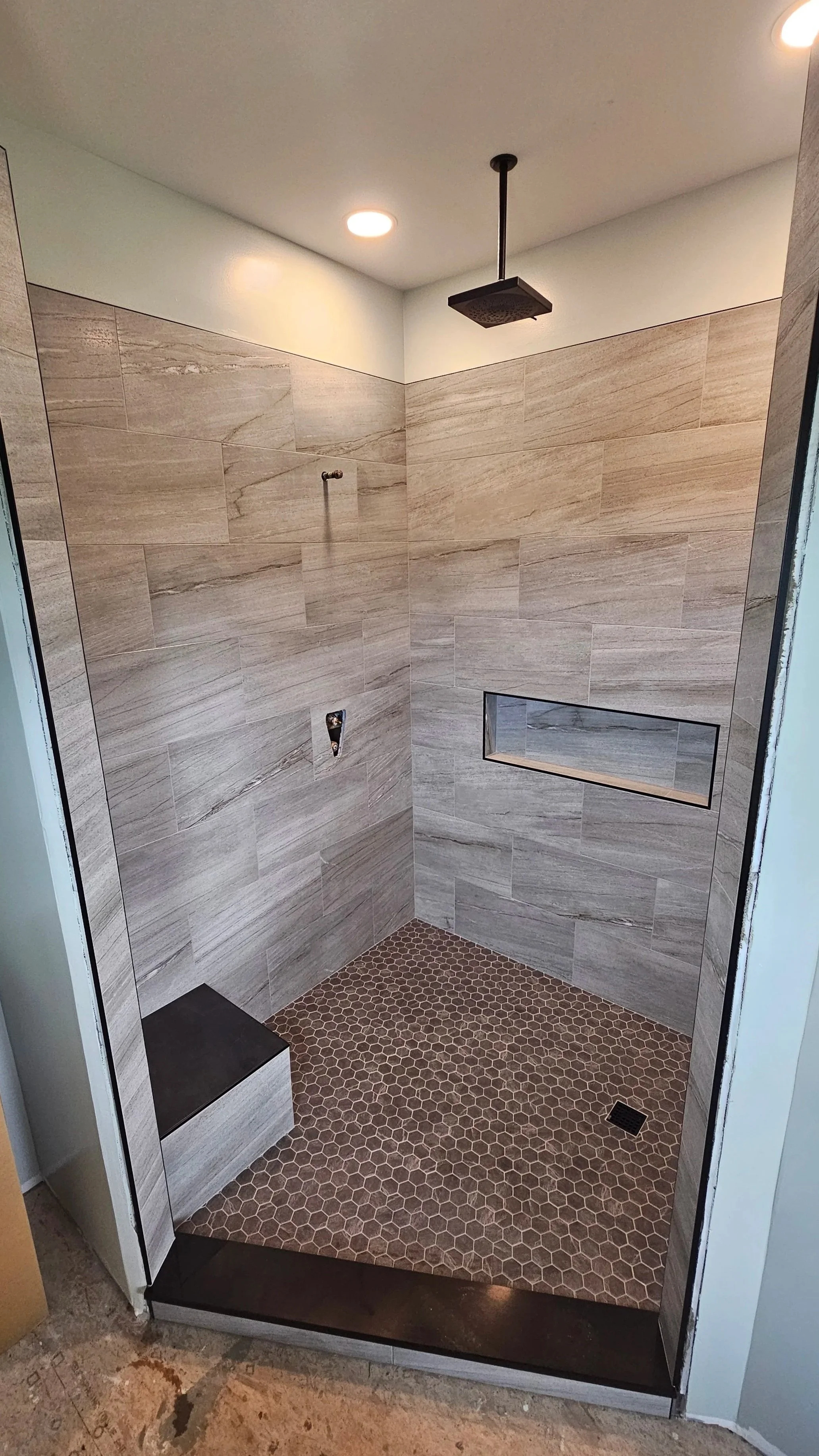 Modern walk-in shower with beige wood-look tile walls, small brown hexagon tile floor, and a ceiling rainfall showerhead.
