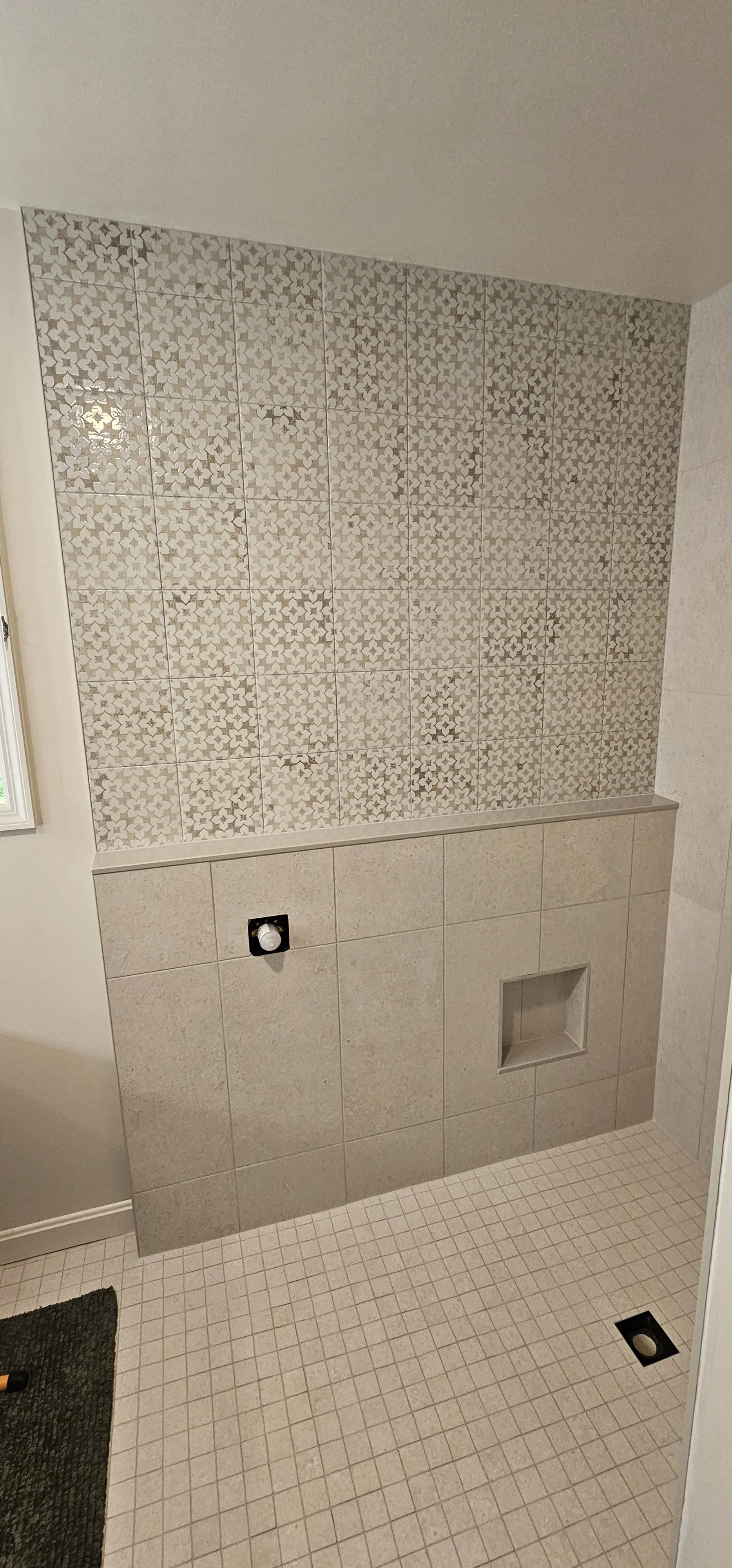 Bathroom shower area with patterned wall tiles, beige lower wall tiles, and a shower niche. Floor has small beige tiles.