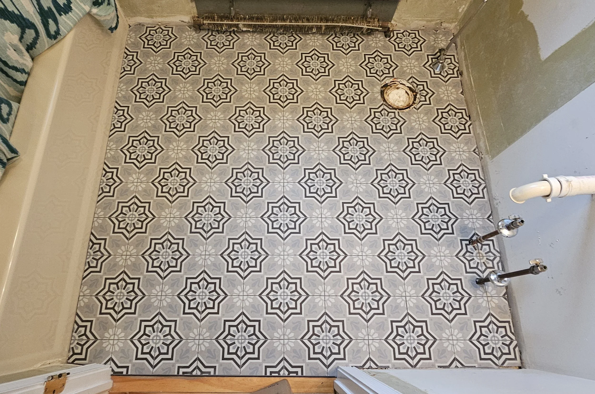 Patterned black-and-white geometric tile floor in a room with unfinished walls and visible piping.
