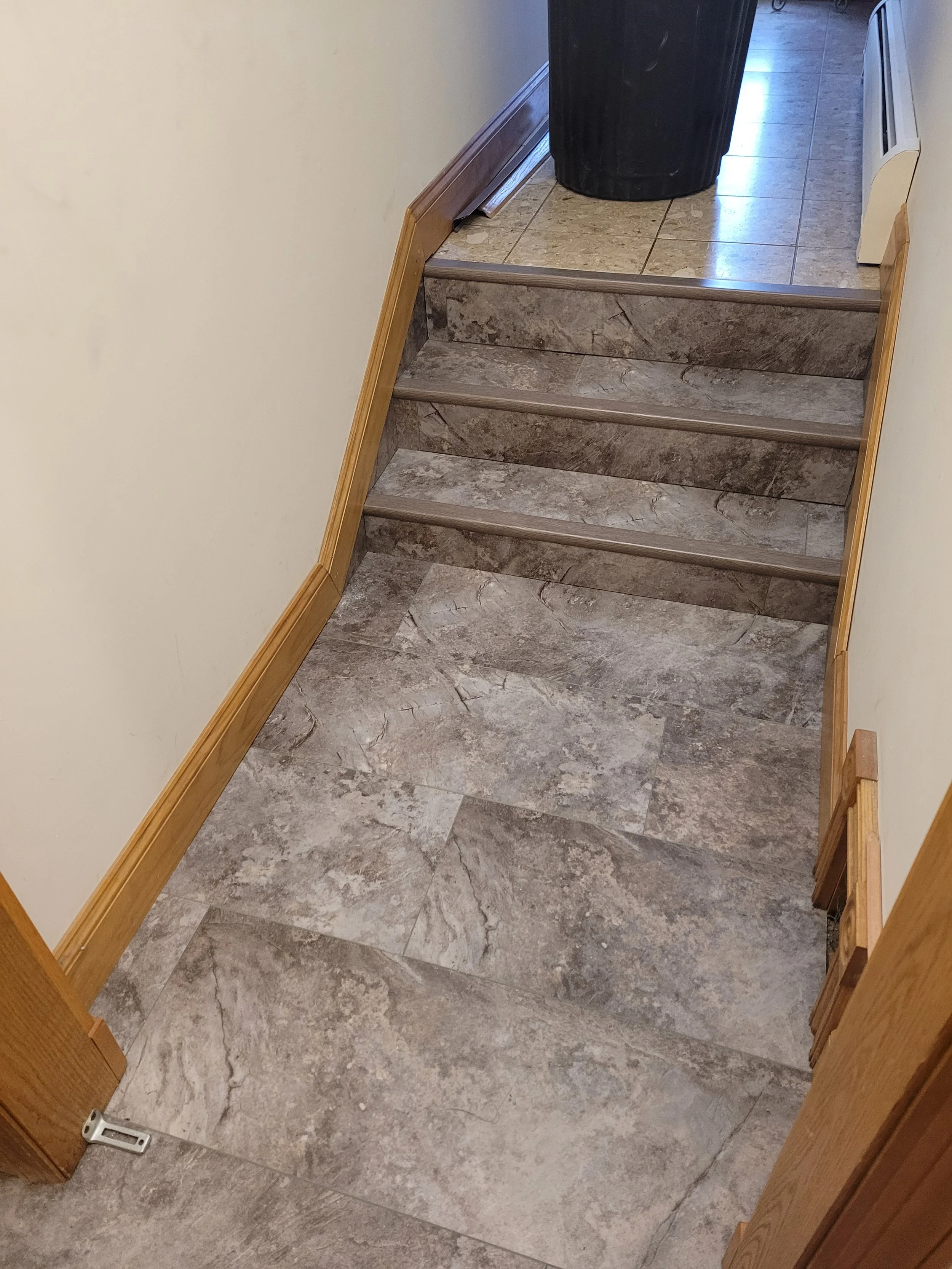 View of a set of marble-like tiled stairs and floor in a hallway, with wooden doorframes on the sides, a vent on the right wall, and a black trash can at the top of the stairs.