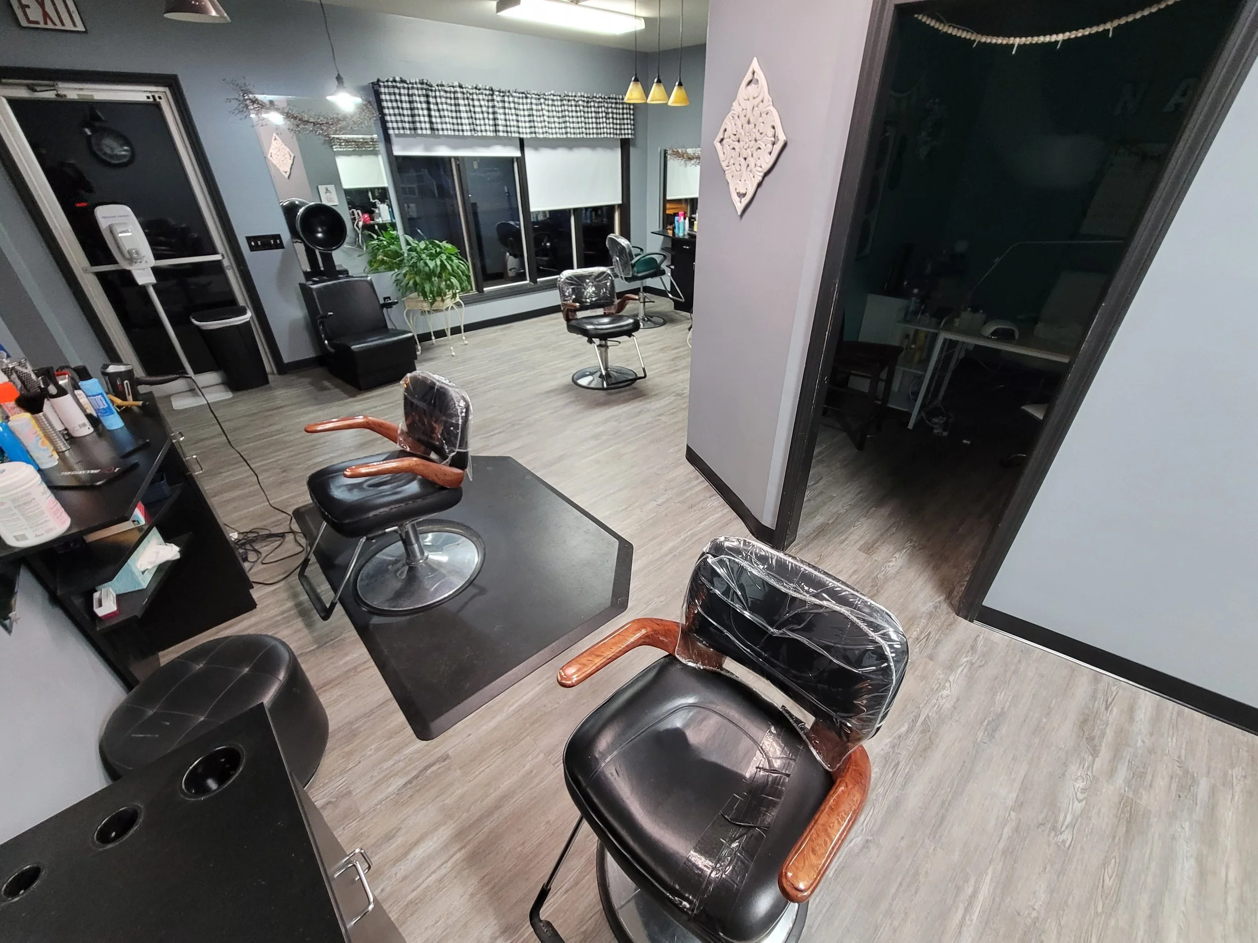Salon with chairs and mirrors, hair styling stations, window with checkered valance, and salon equipment.