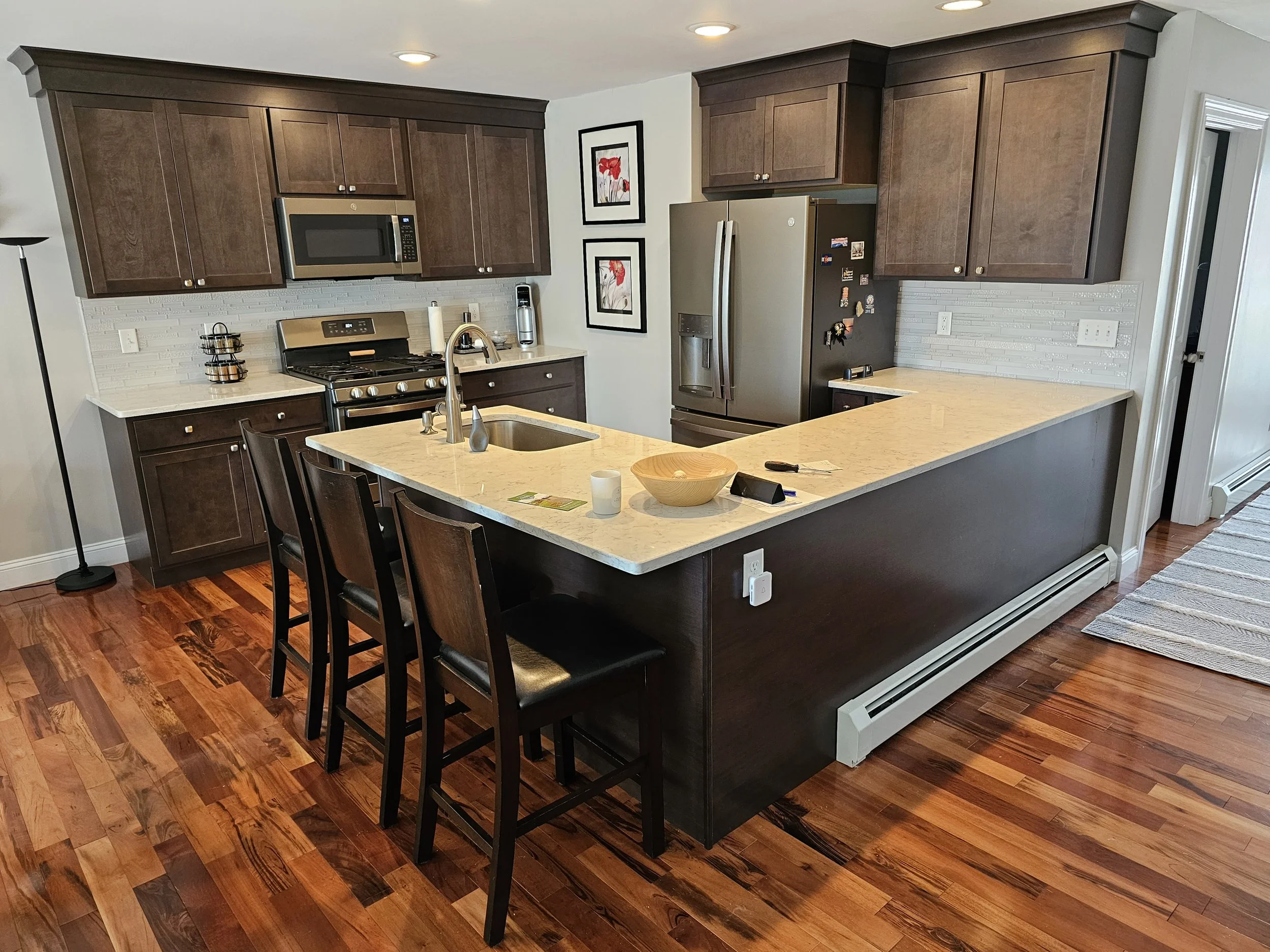 Modern kitchen with granite island, dark wood cabinets, stainless steel appliances, hardwood floors, and decorative artwork on the wall.