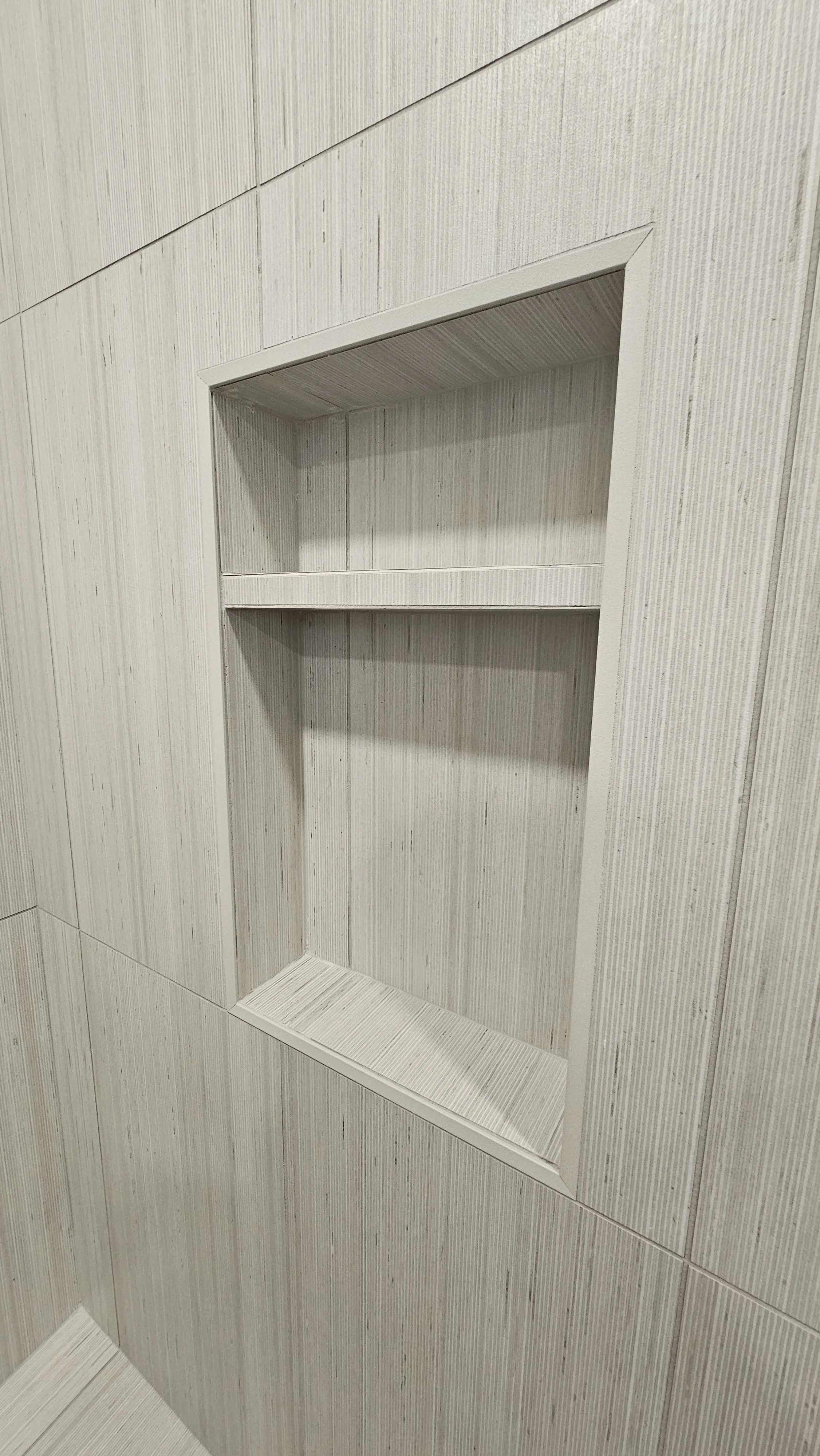 Built-in corner shower niche with tiled interior in a bathroom with light-colored tiled walls.
