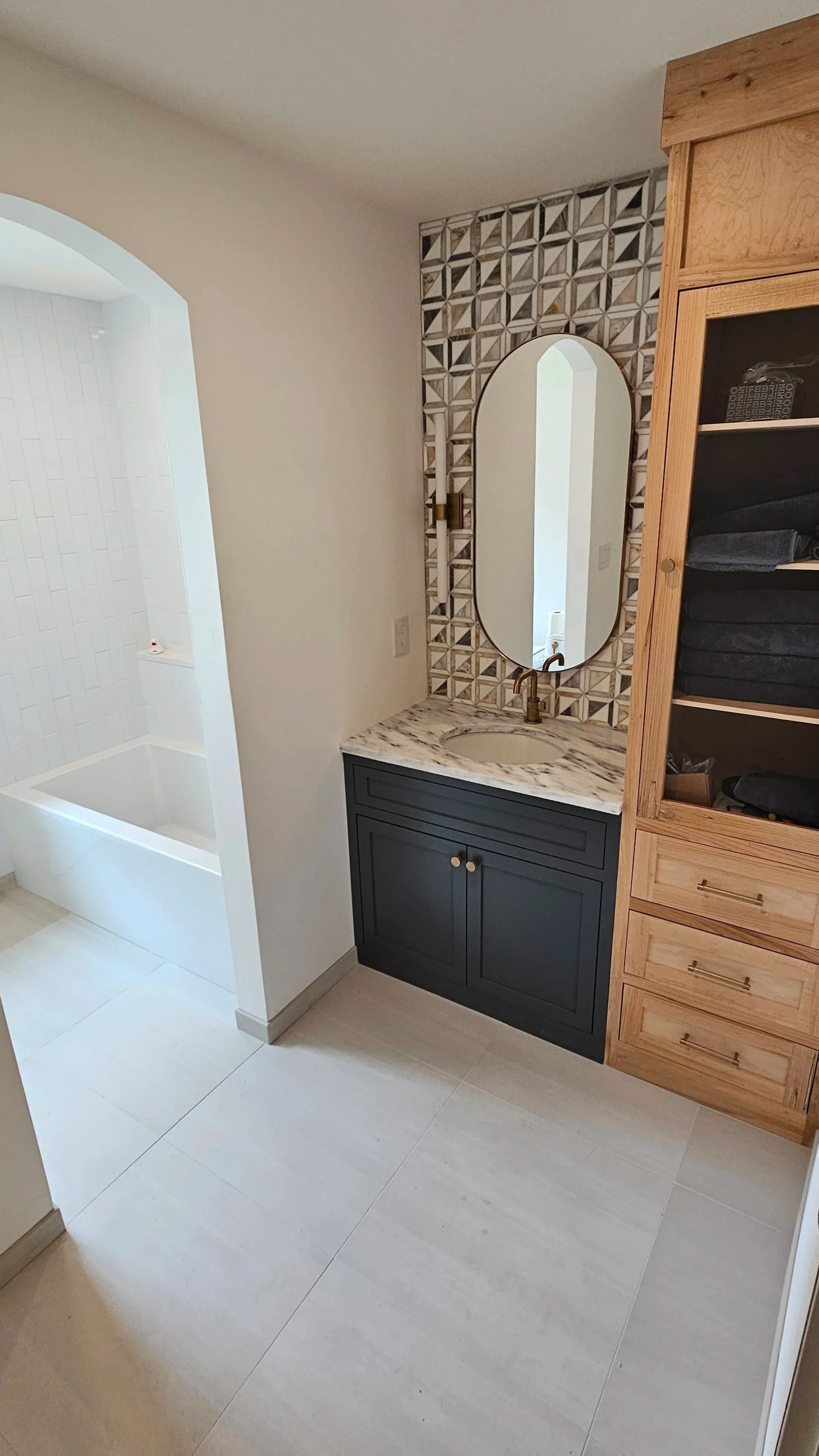 Bathroom with a shower area, sink with dark blue cabinet, vanity mirror, and a wooden cabinet with towels.