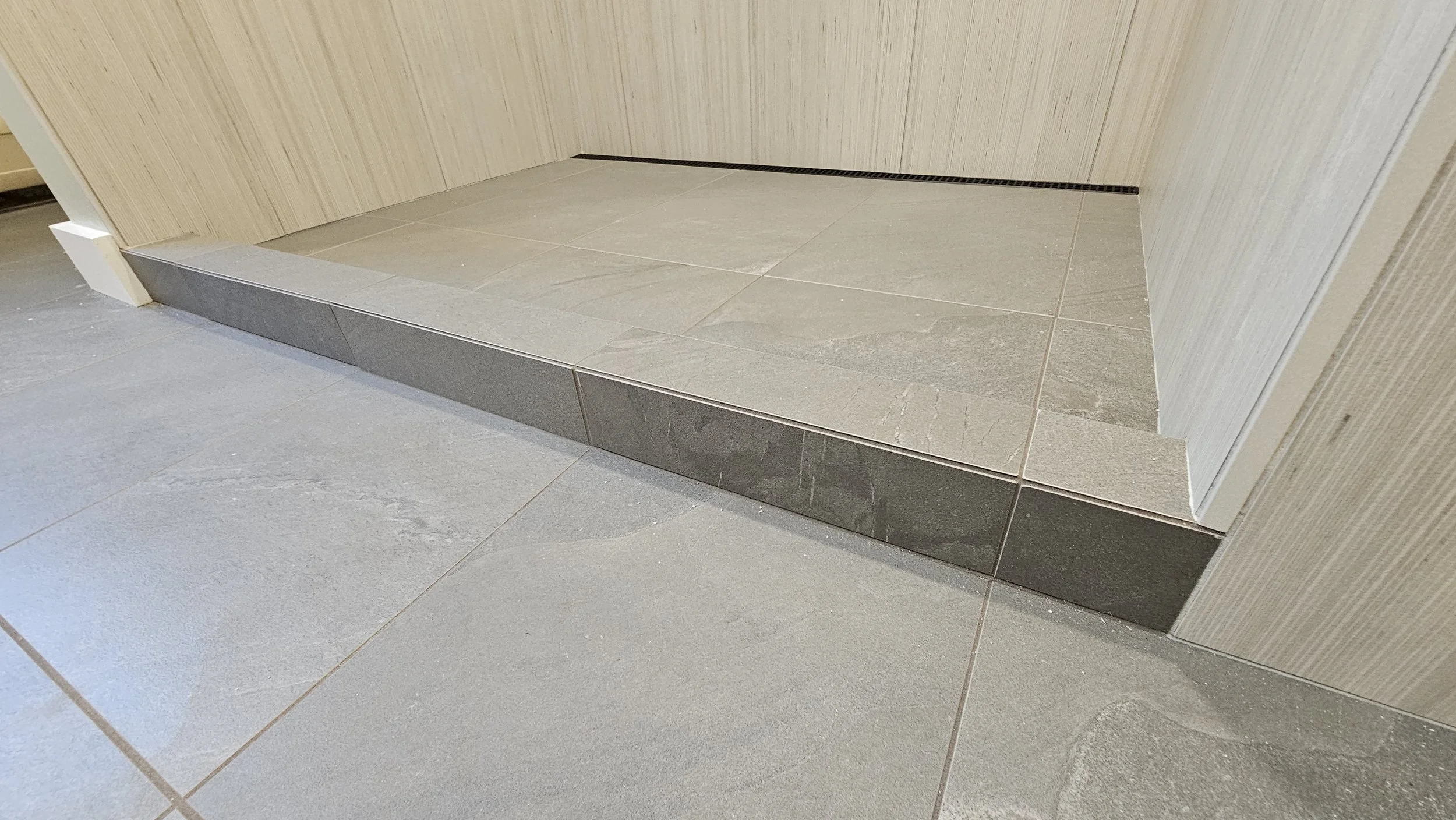 Close-up of a tiled shower base with a partial wall and a corner drain.
