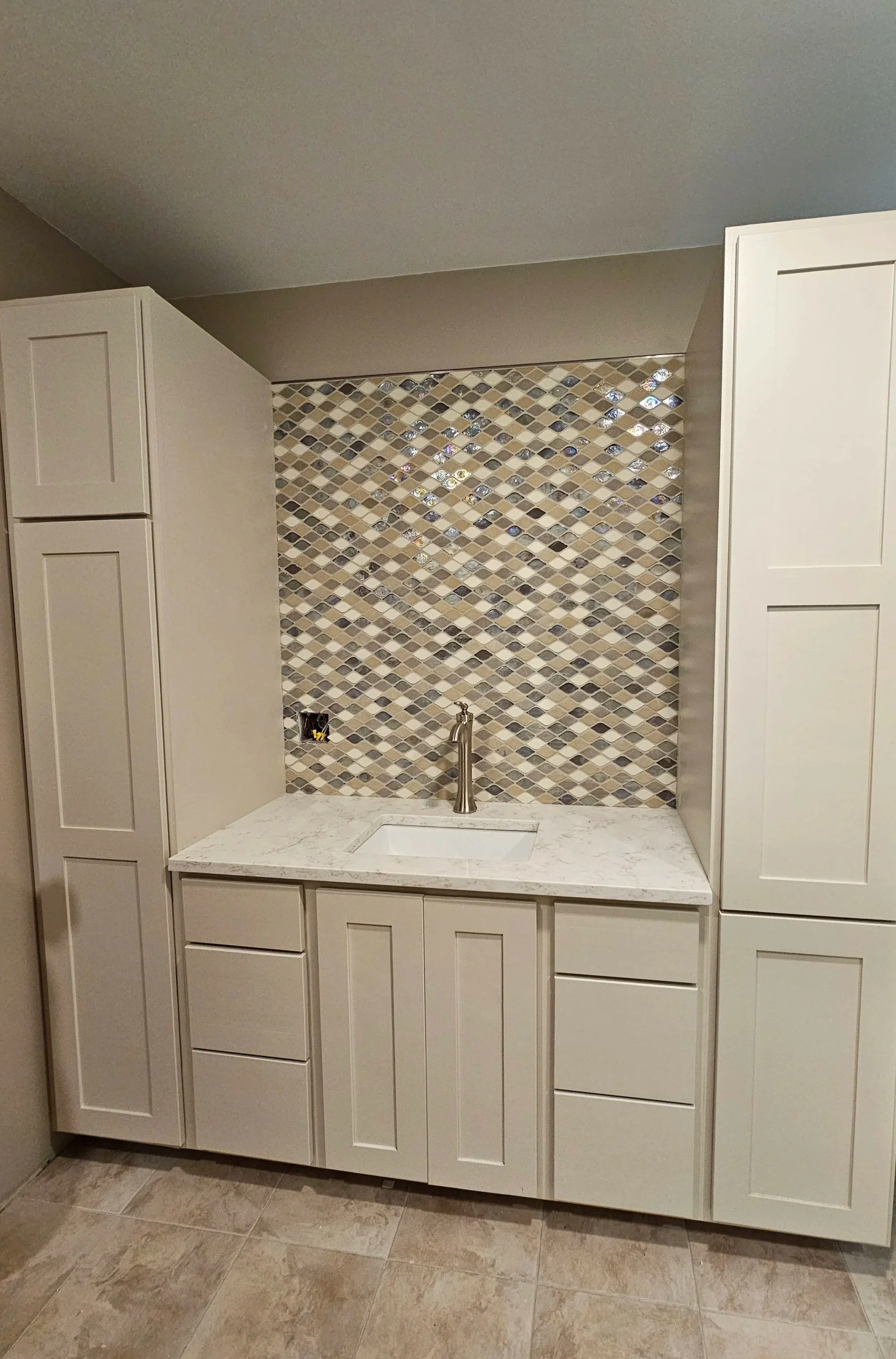 Bathroom with white cabinets, mosaic tile backsplash, marble countertop, and a sink with a silver faucet.