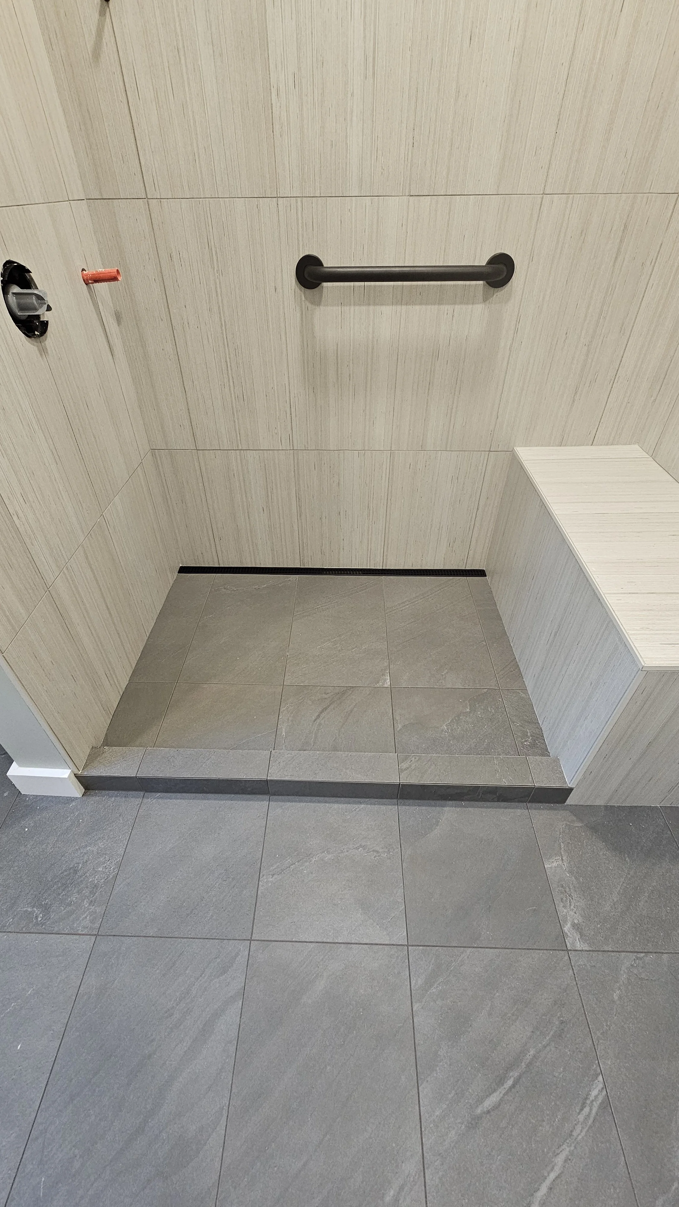 Empty handicapped accessible shower with grab bar, tiled walls and floor, and a small bench.