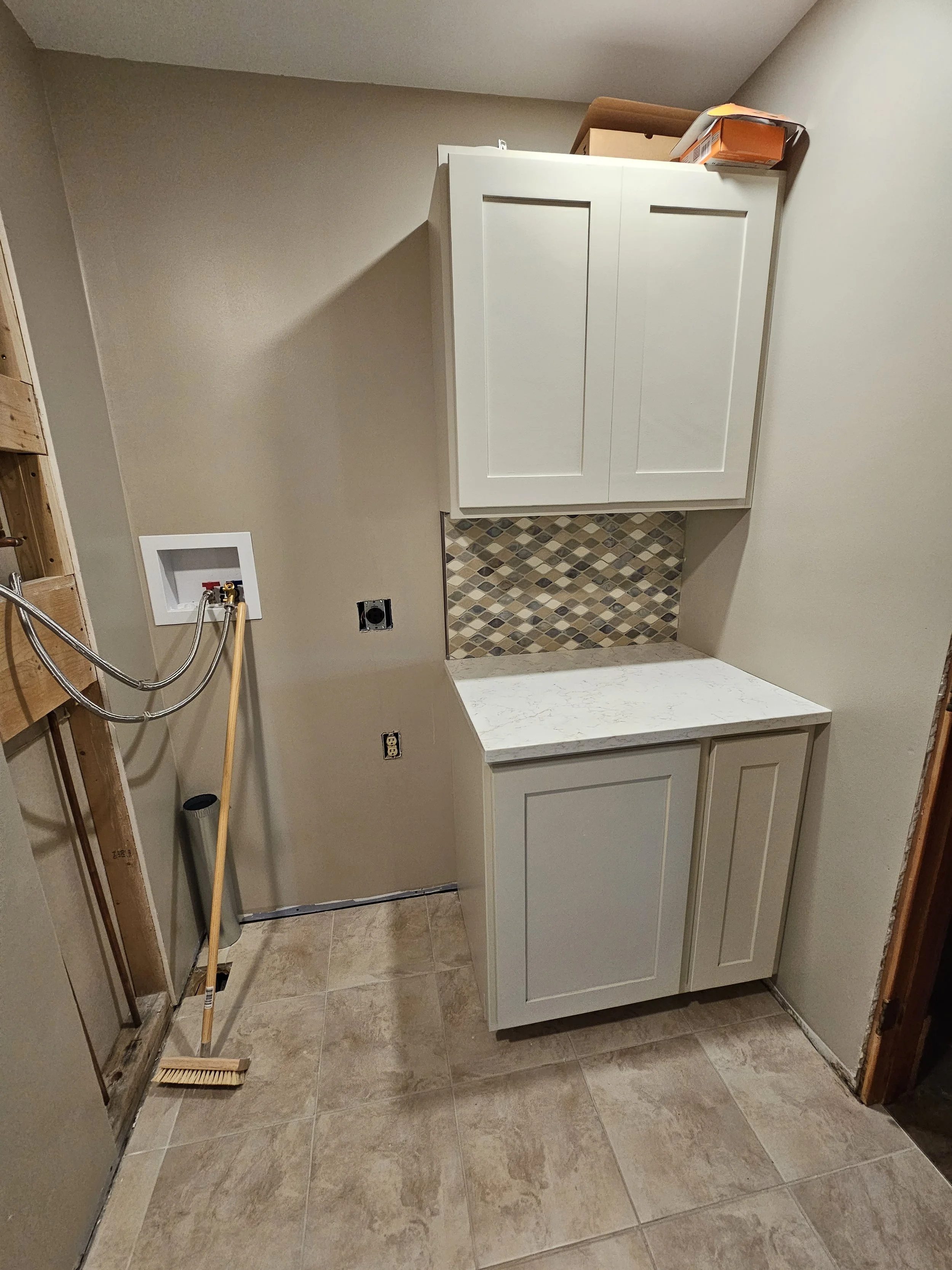 Bathroom with a white cabinet, tiled backsplash, beige walls, beige tiled floor, and construction tools including a broom and mop.