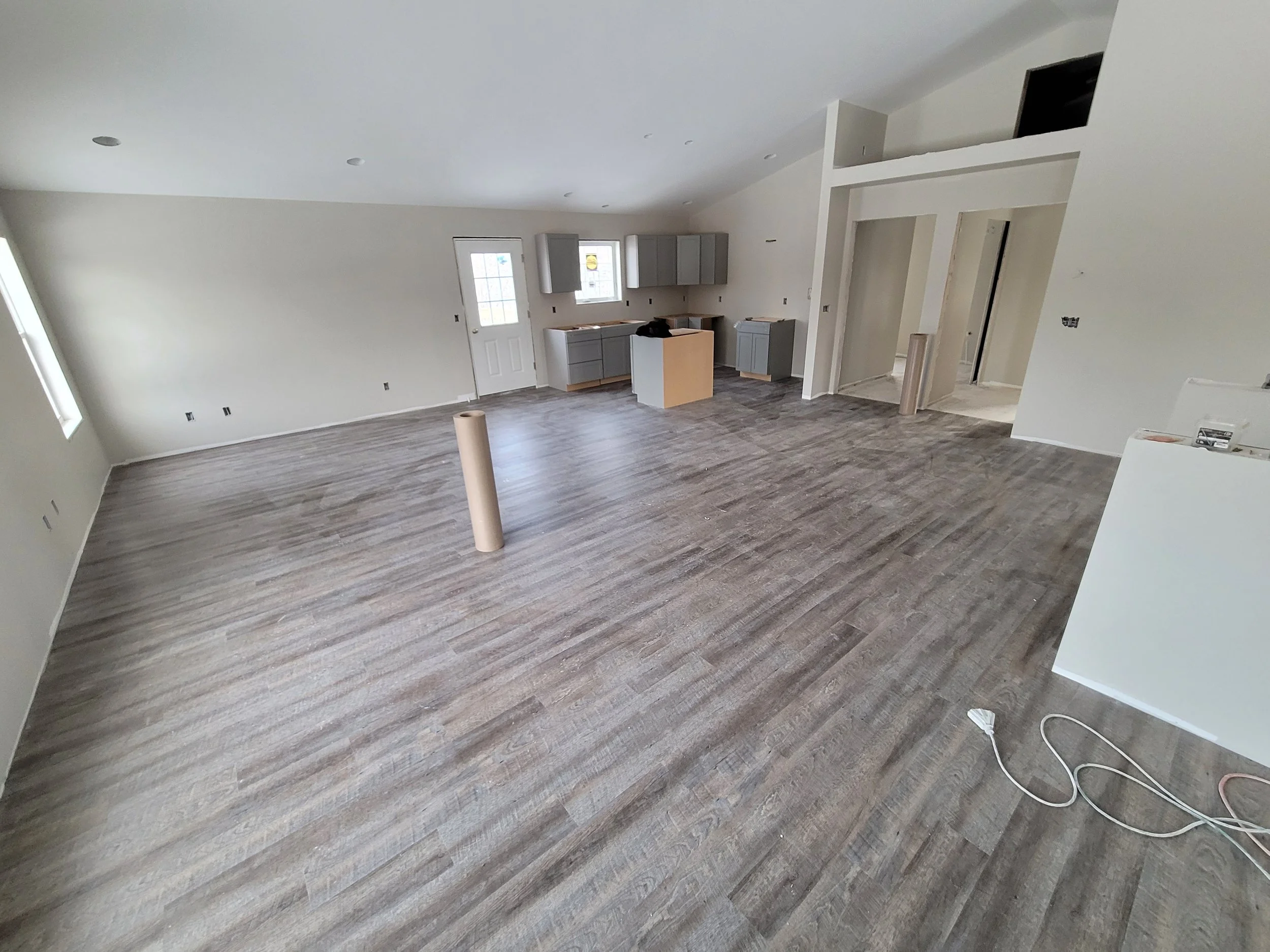 Empty room under construction with wooden flooring, unfinished cabinets, and construction materials.