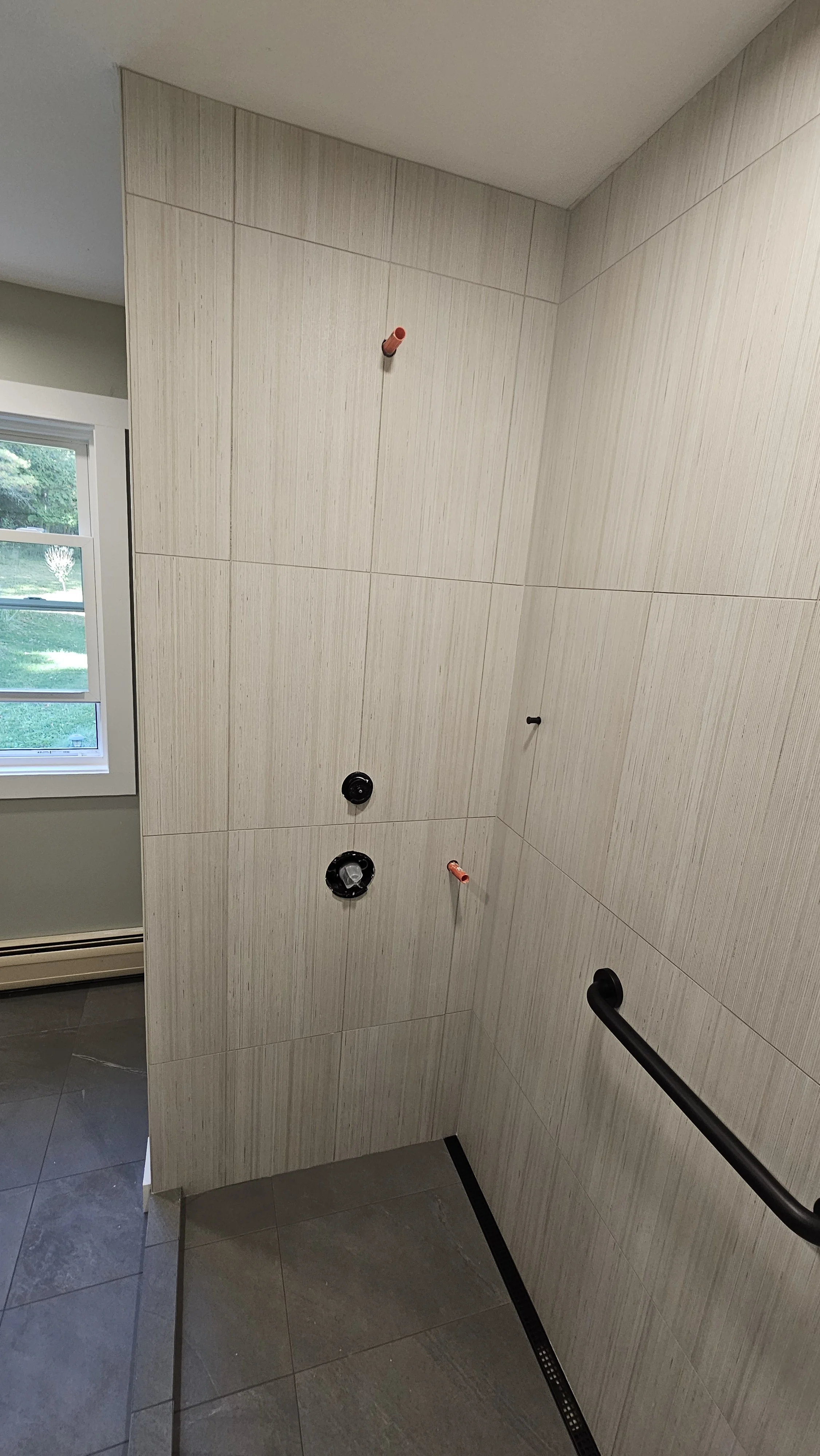 Bathroom wall with plumbing fixtures and fixtures for a shower installation in progress.