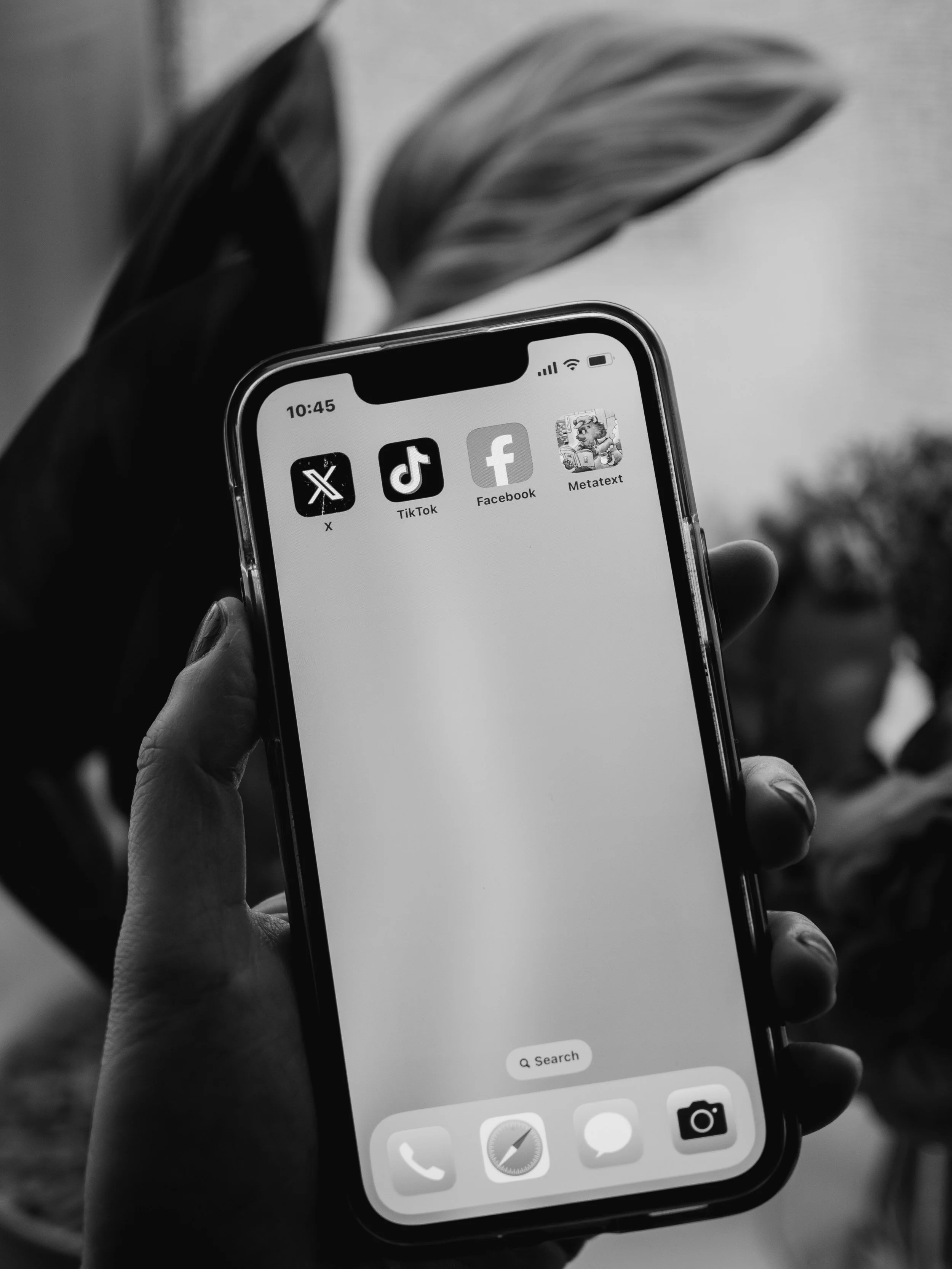 Imagen en blanco y negro de un teléfono inteligente en la mano de una persona, mostrando las aplicaciones de X, TikTok, Facebook y Metatext en la pantalla.