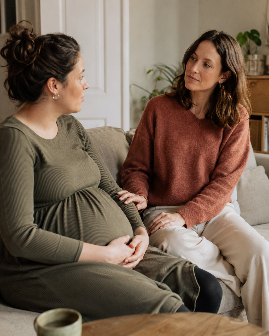 Een doula luistert aandachtig naar een zwangere vrouw tijdens een gesprek thuis.