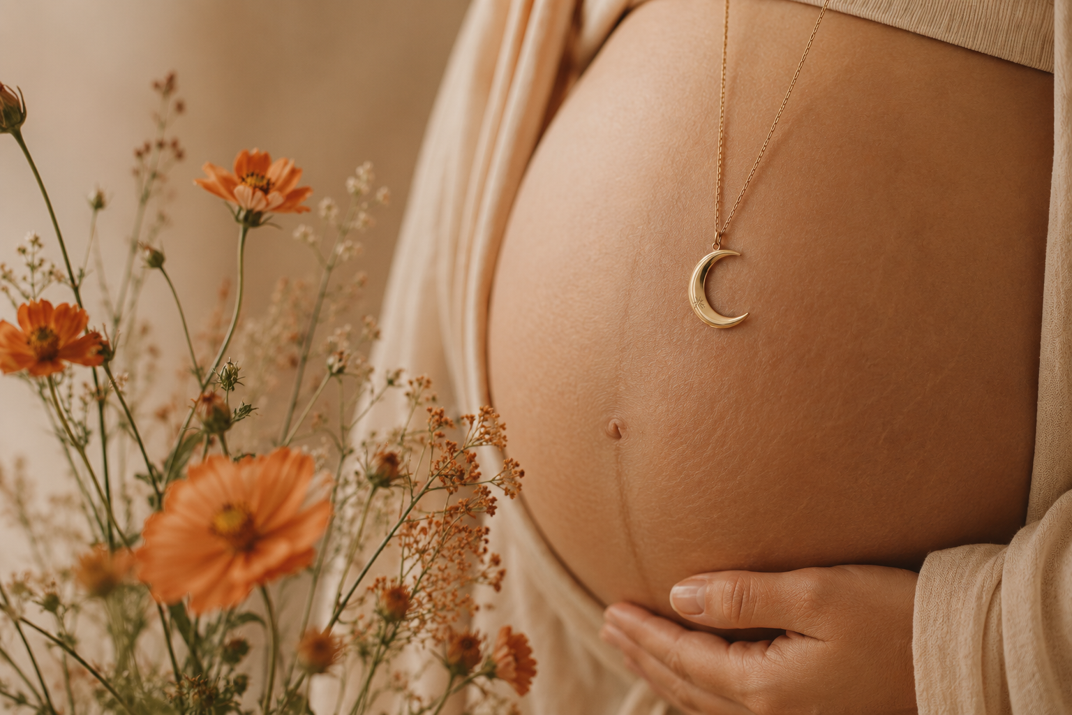 Zwangere vrouw met maanketting tussen oranje bloemen bij Mothers & Moon