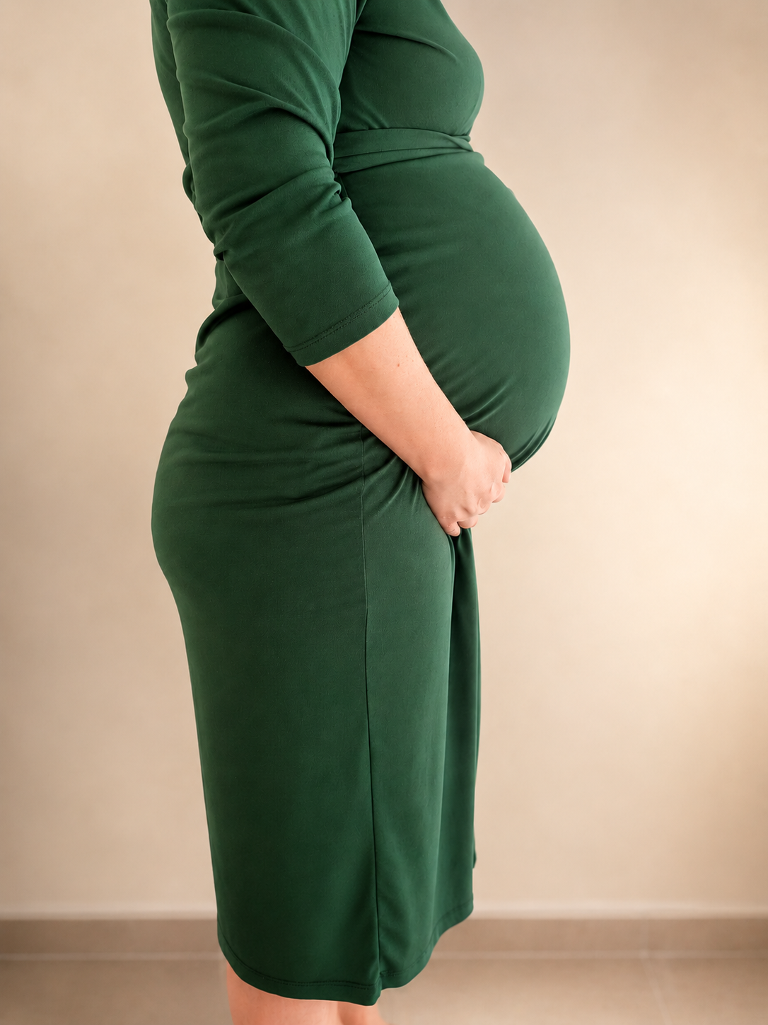 Zwangere vrouw in een groene jurk houdt haar buik vast