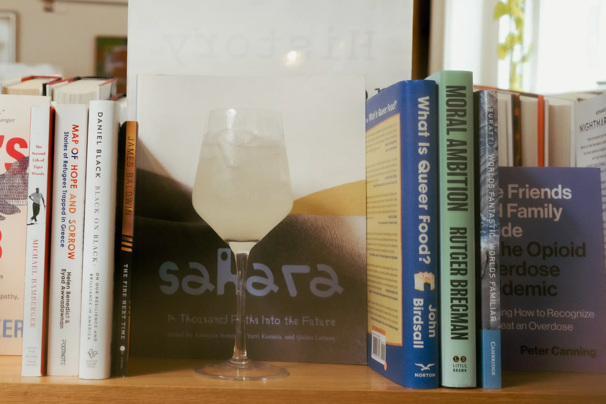 A glass of water placed on a bookshelf in front of a row of various books.