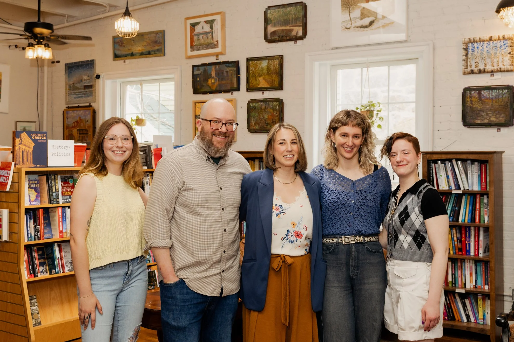 Group of five people smiling and posing inside a bookstore, with bookshelves and framed artwork on the wall behind them.