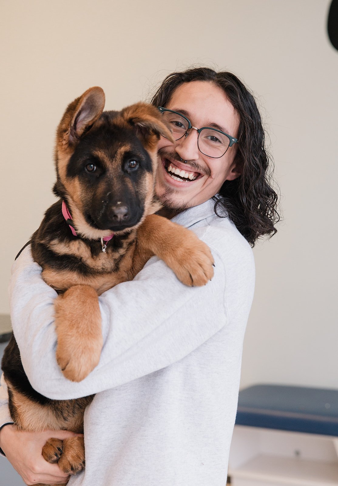 A person with glasses and long dark hair holding a German Shepherd puppy