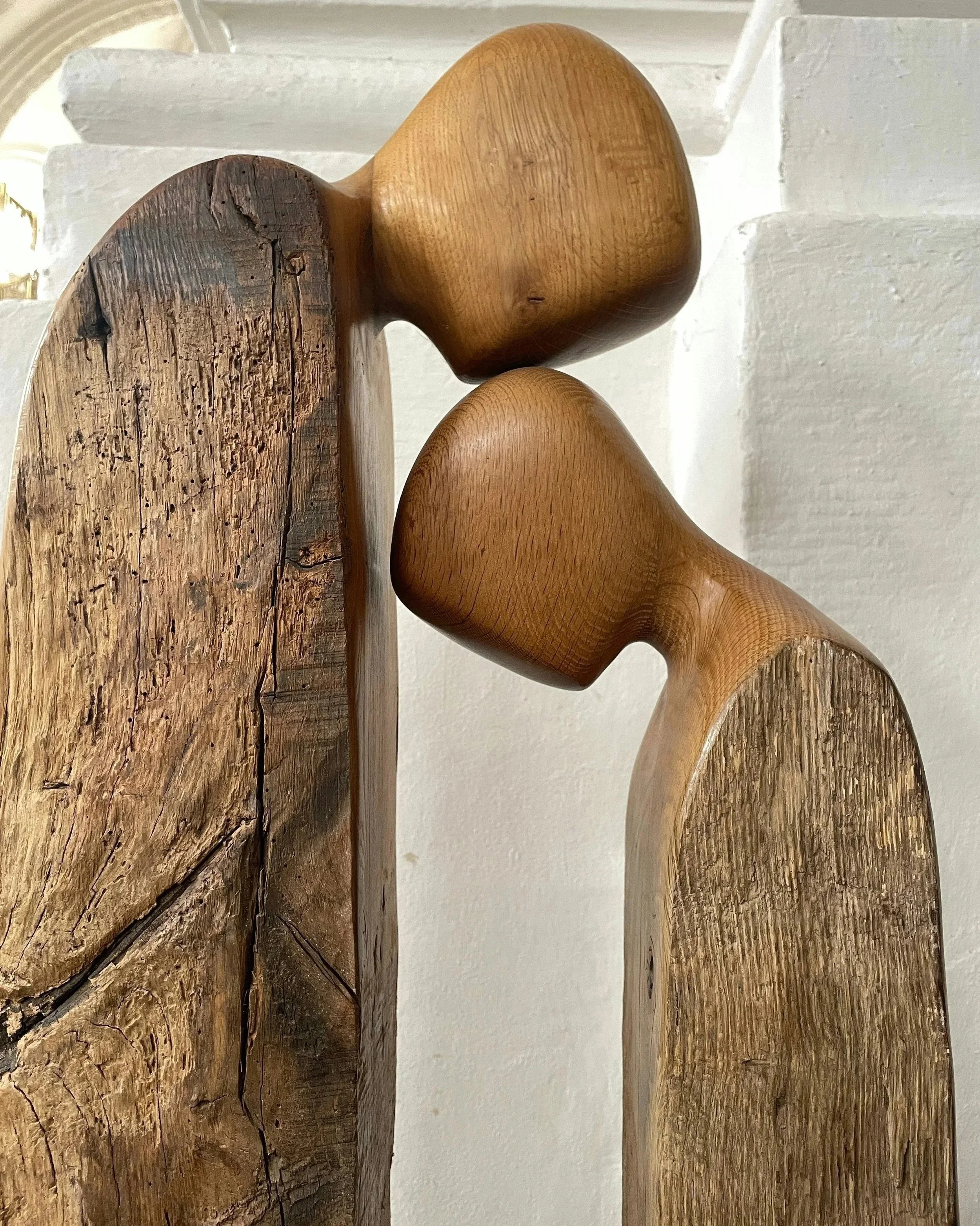 Close-up of wooden chair legs with different textures, some smooth and polished, others rough and weathered, against a plain white wall.