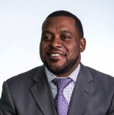 A man in a dark suit and purple tie posing for a professional photo.