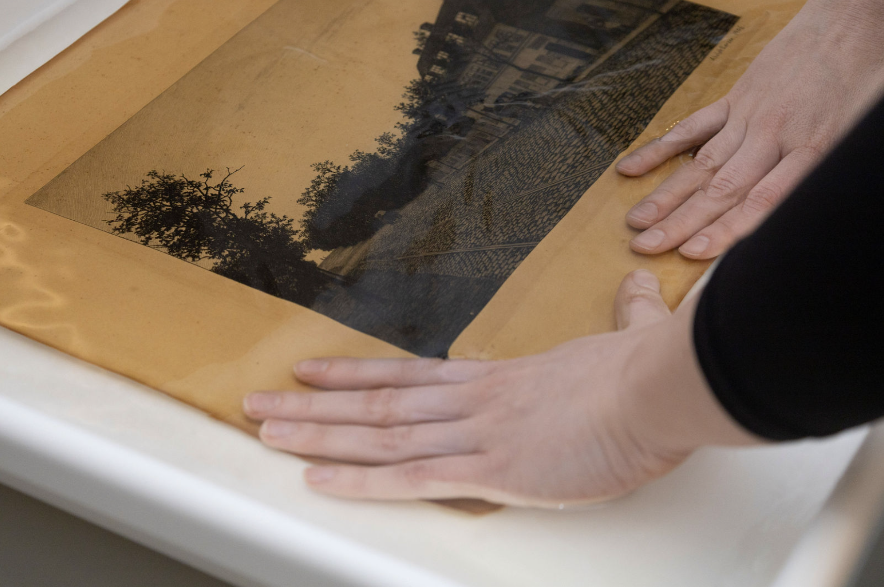 Person with hands submerged in water, washing an old print.