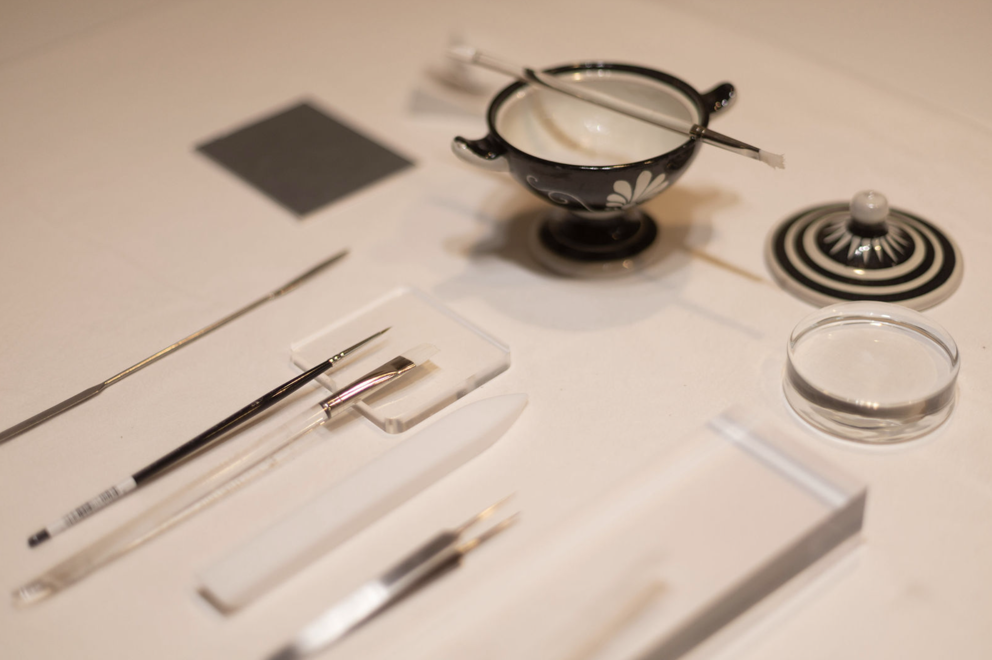 Conservation tools on a white table including a black and white decorative bowl, paint brushes, scalpels, and weights.