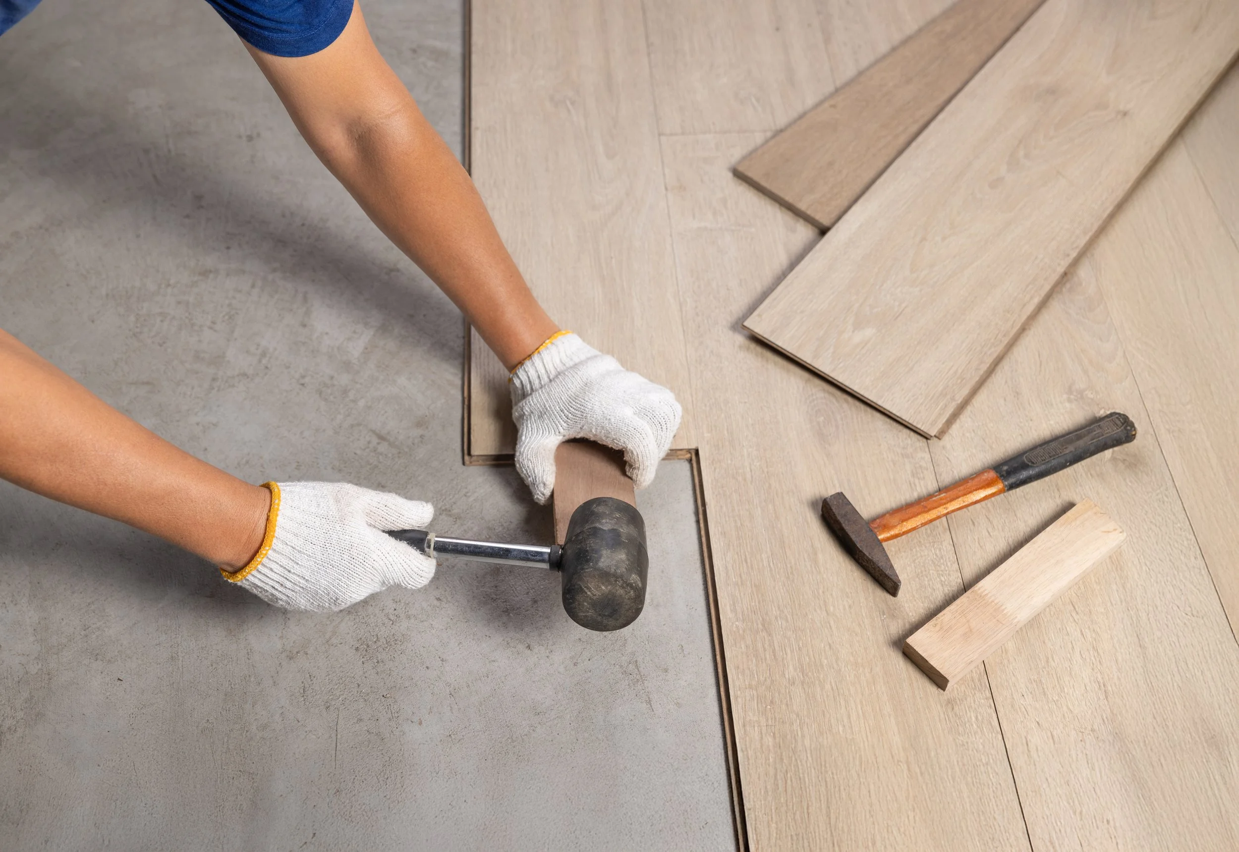 Person installing wood flooring using a mallet, with several wood planks laid out on the floor, and tools nearby.