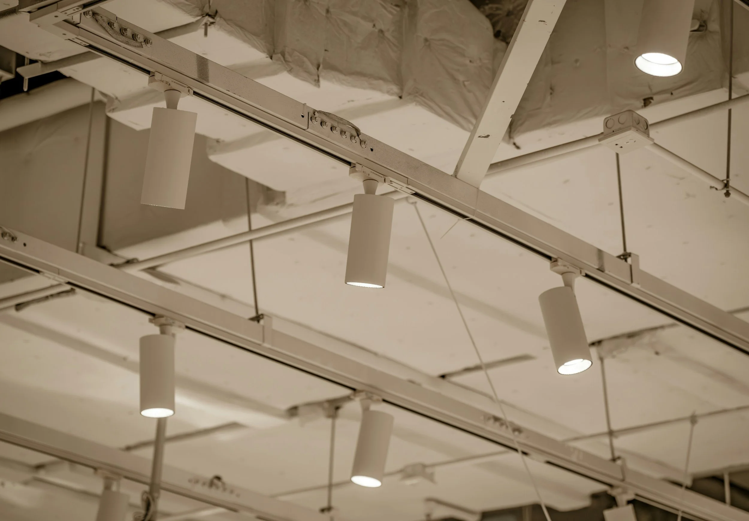 Ceiling with mounted track lighting fixtures and ceiling panels, some with visible insulation.