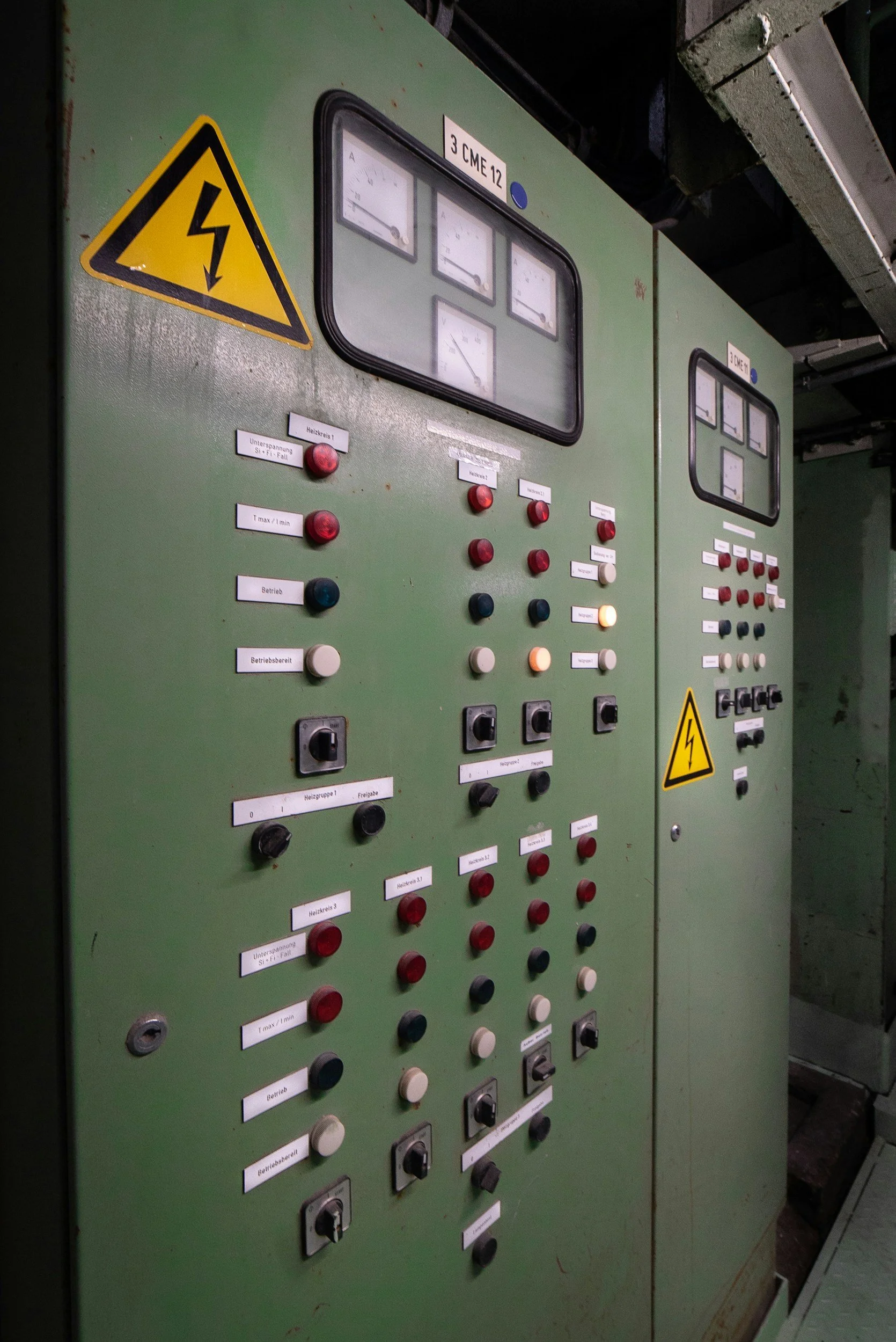 Electrical control panels with multiple switches, dials, and meters, labeled in German, featuring warning signs with lightning bolt symbols indicating electrical hazard.