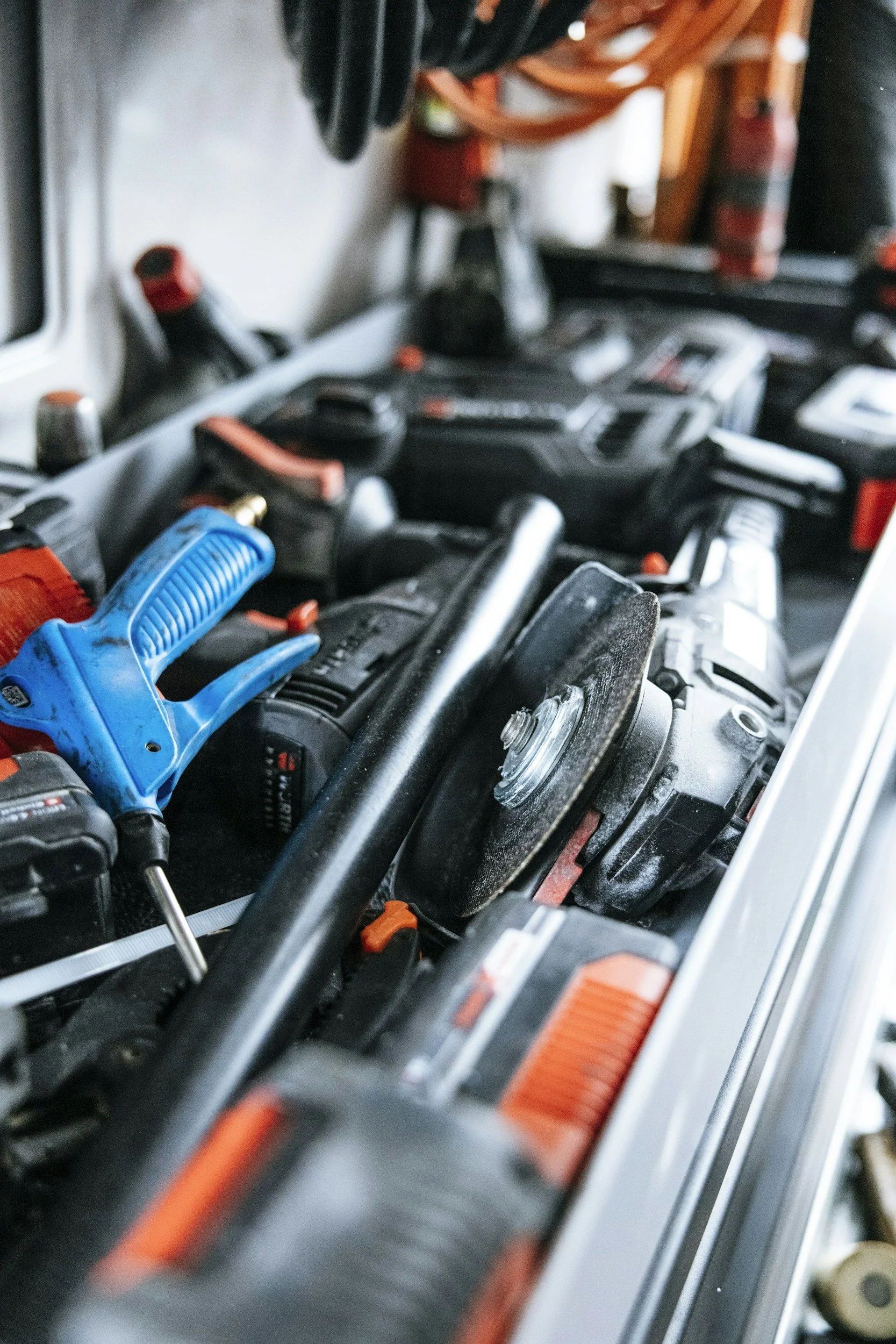 A close-up view of a workbench with various cordless power tools and accessories, including a blue plastic clamp, a drill, and what appears to be a cordless screwdriver, along with some chemical containers and an extension cord.