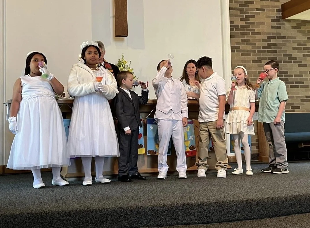 Children in formal and semi-formal attire standing on a church stage, participating in a ceremony or celebration.