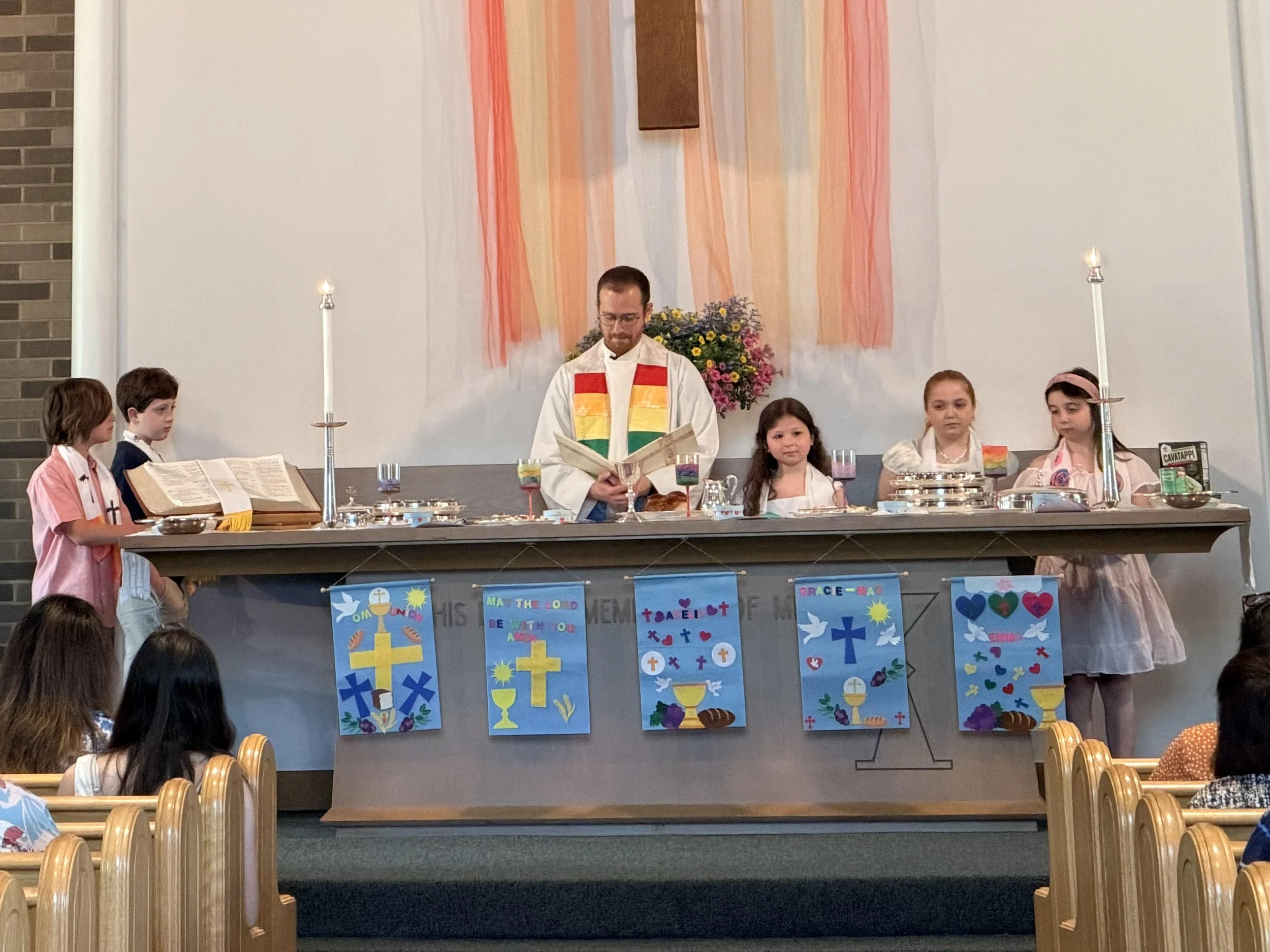 Children in formal and semi-formal attire standing on a church stage, participating in a ceremony or celebration.