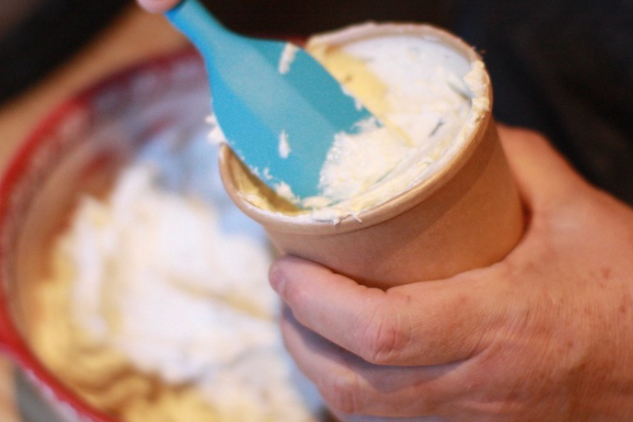 Hand spreading cream cheese schmear onto a bagel, fatbaby Bakes