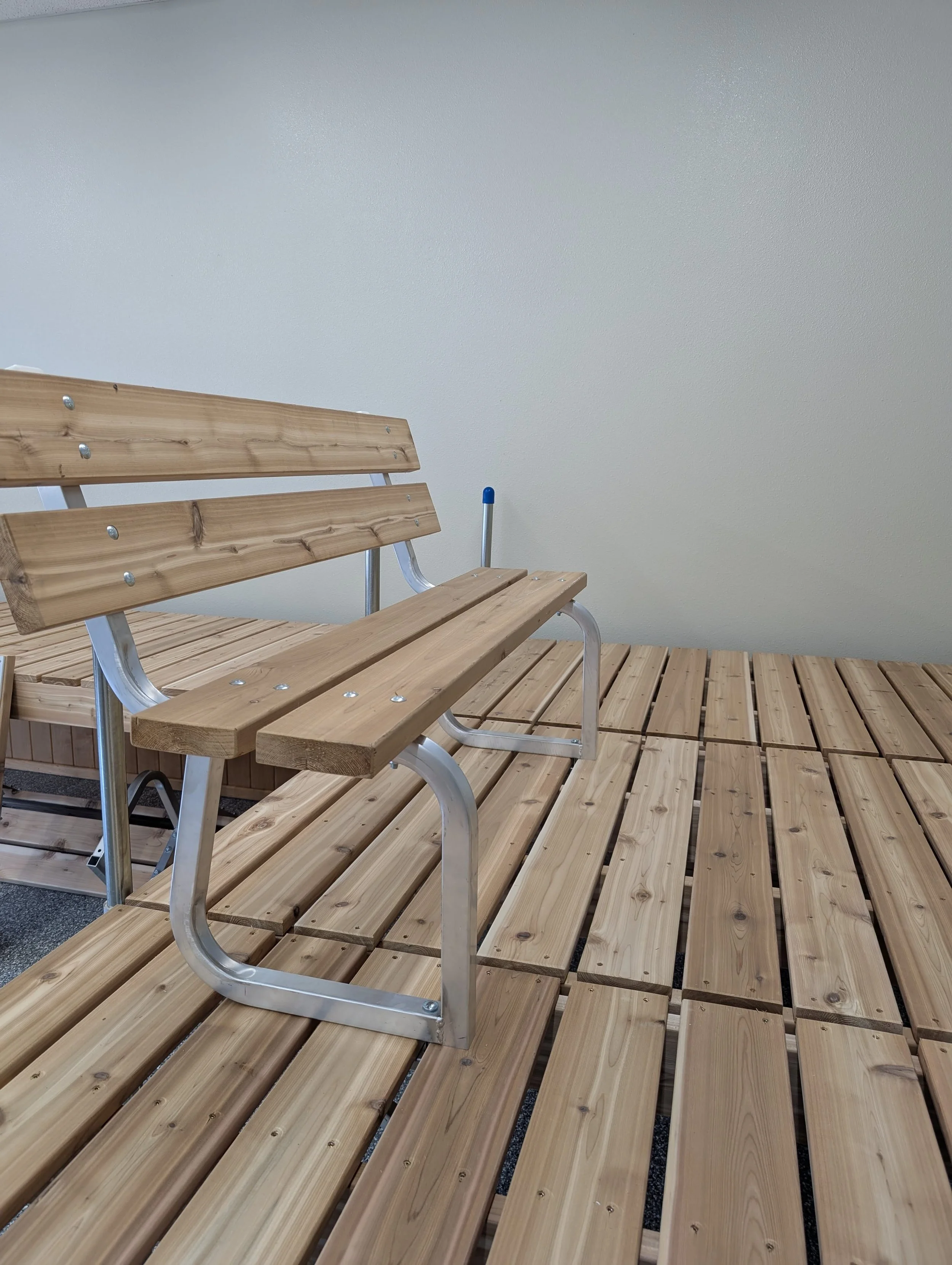 A wooden park bench with a metal frame in front of a plain white wall.