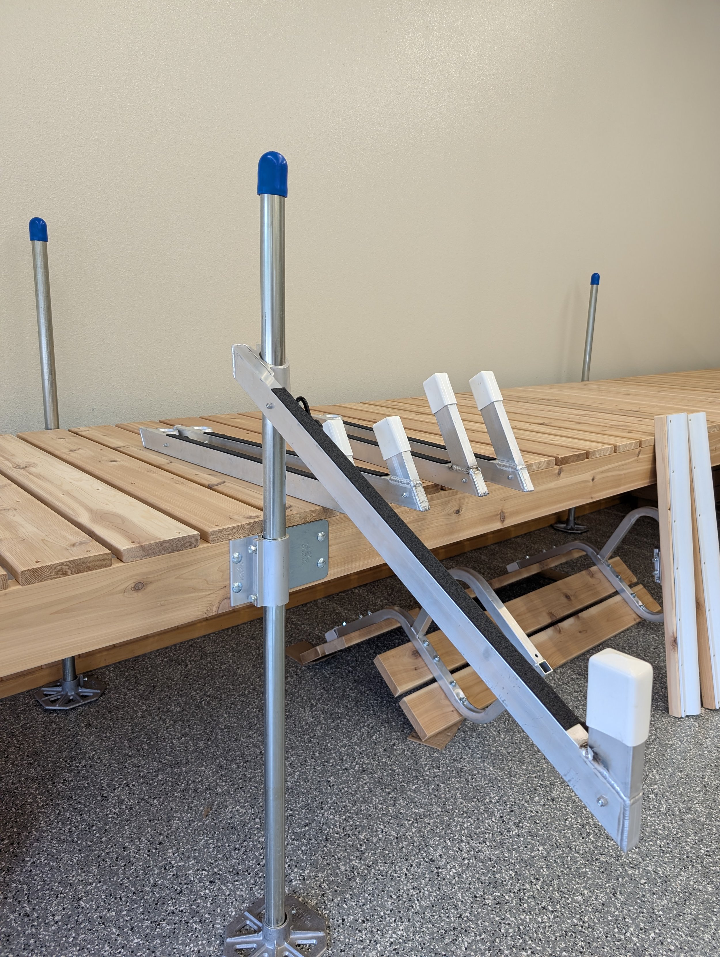 A wooden table with a metal adjustable stand or frame on top, with blue-tipped metal poles sticking up, amid a speckled flooring.