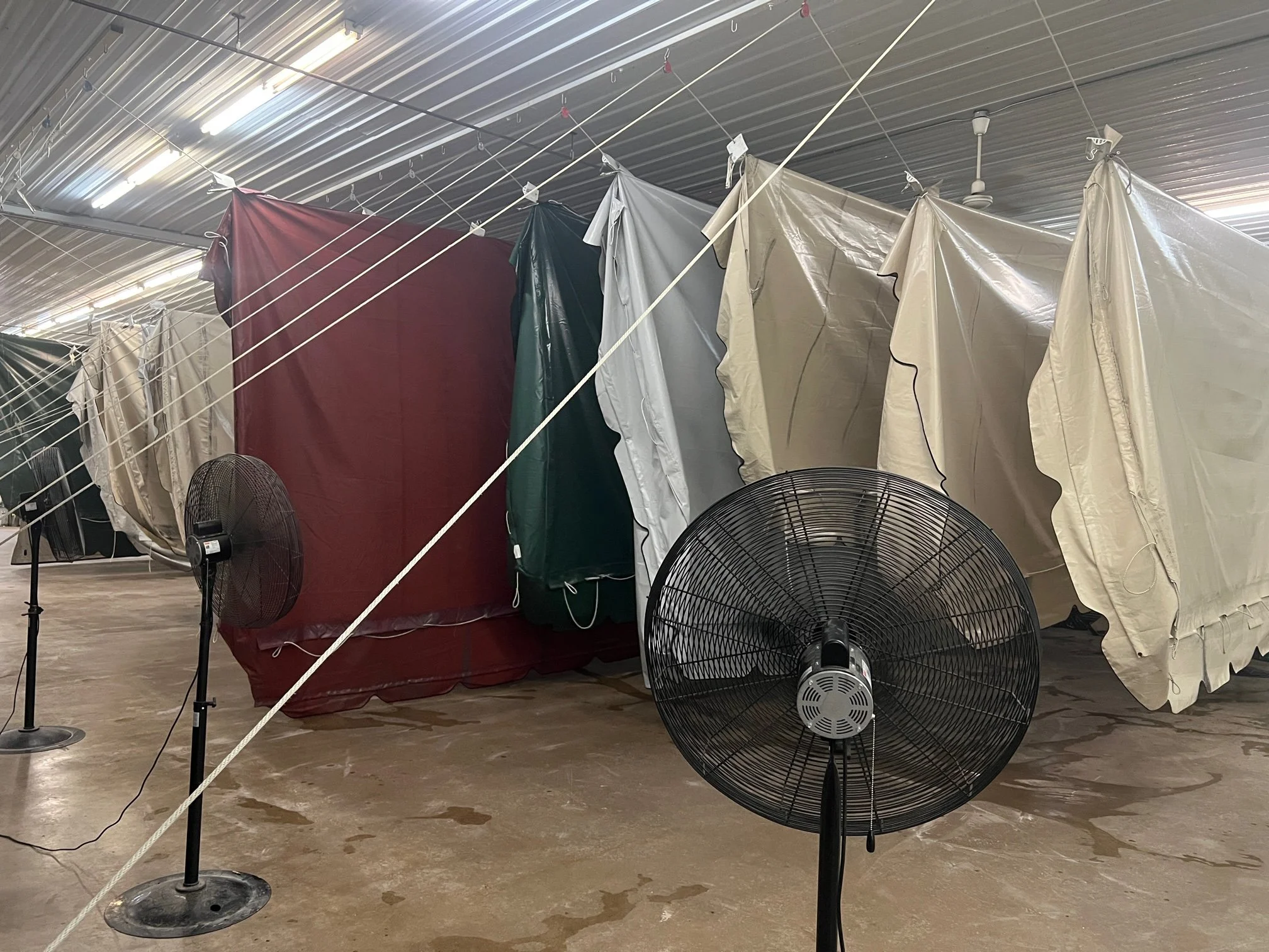 Indoor space with hanging fabrics, fans, and poles with wires strung overhead, possibly a storage or laundry area.