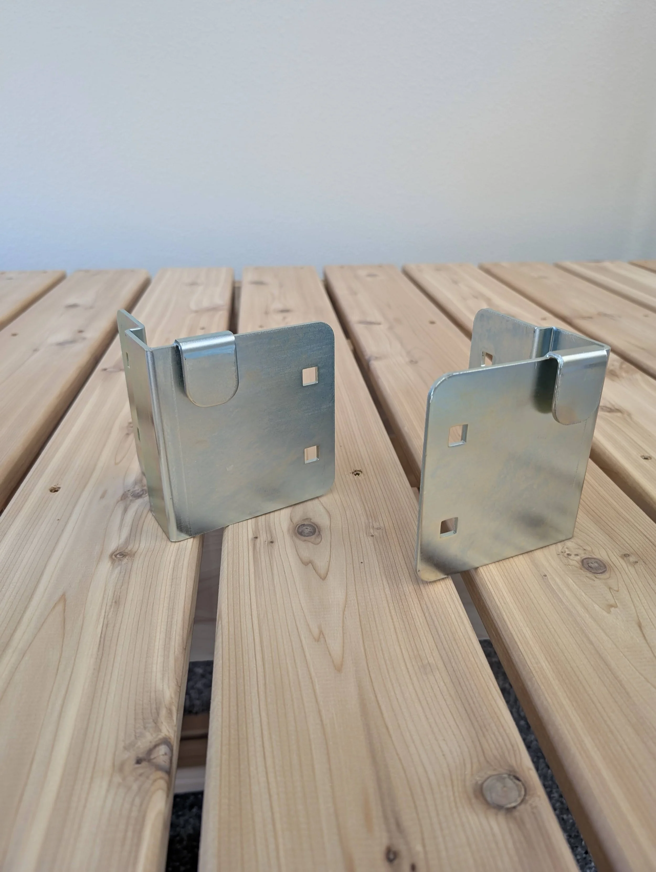 Two metal brackets on a light wooden slatted surface with a white wall in the background.