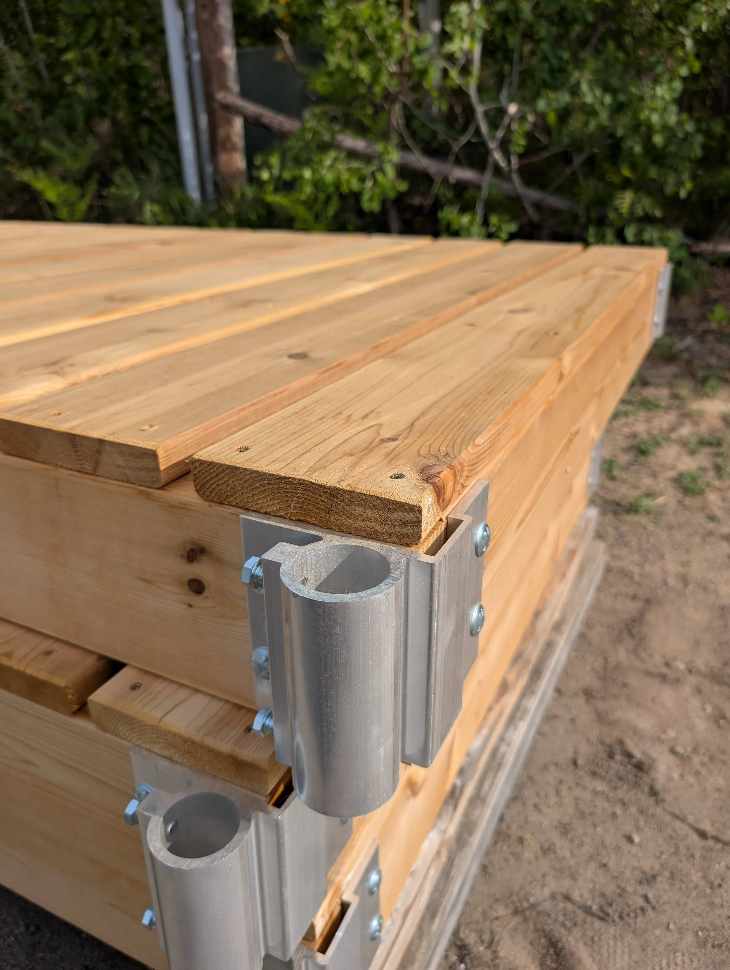 Close-up view of a wooden structure with metal brackets and bolts, with leafy green trees in the background.