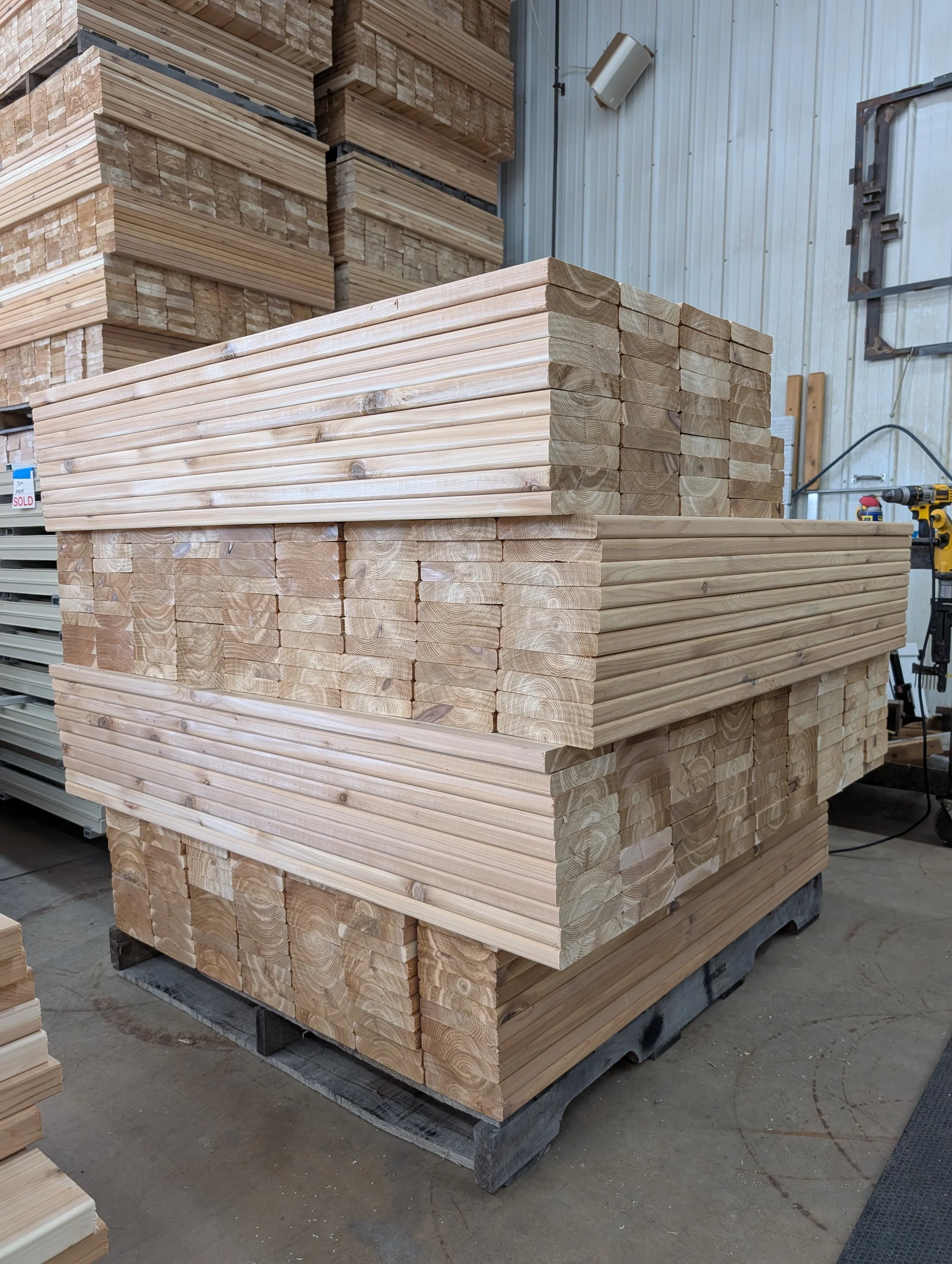 Stacks of lumber in a warehouse or storage facility with some wood pieces stacked on a pallet and others on shelves in the background.