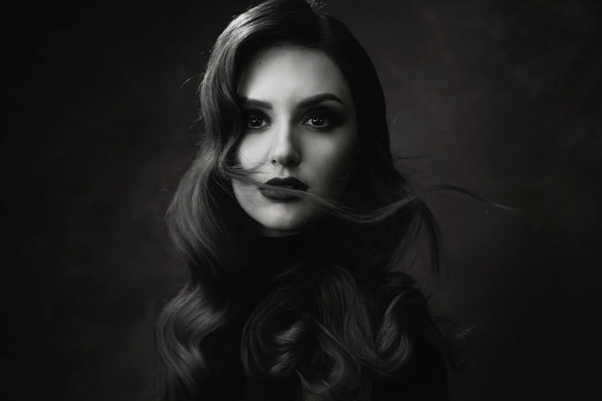 Ritratto in bianco e nero di modella dai capelli lunghi e ricci con sguardo intenso.
