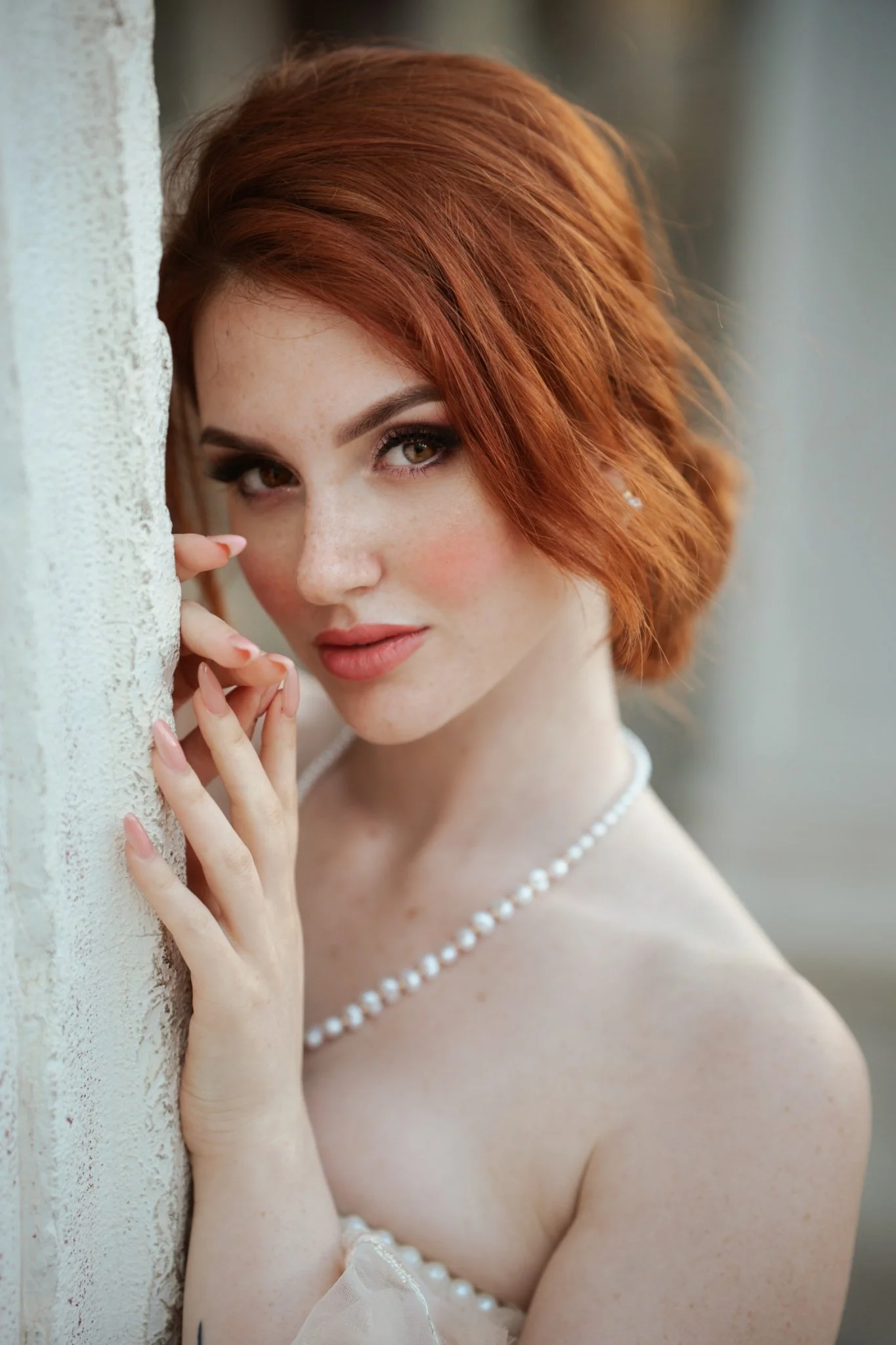 Ritratto elegante di modella dai capelli rossi con collana di perle e abito chiaro.
