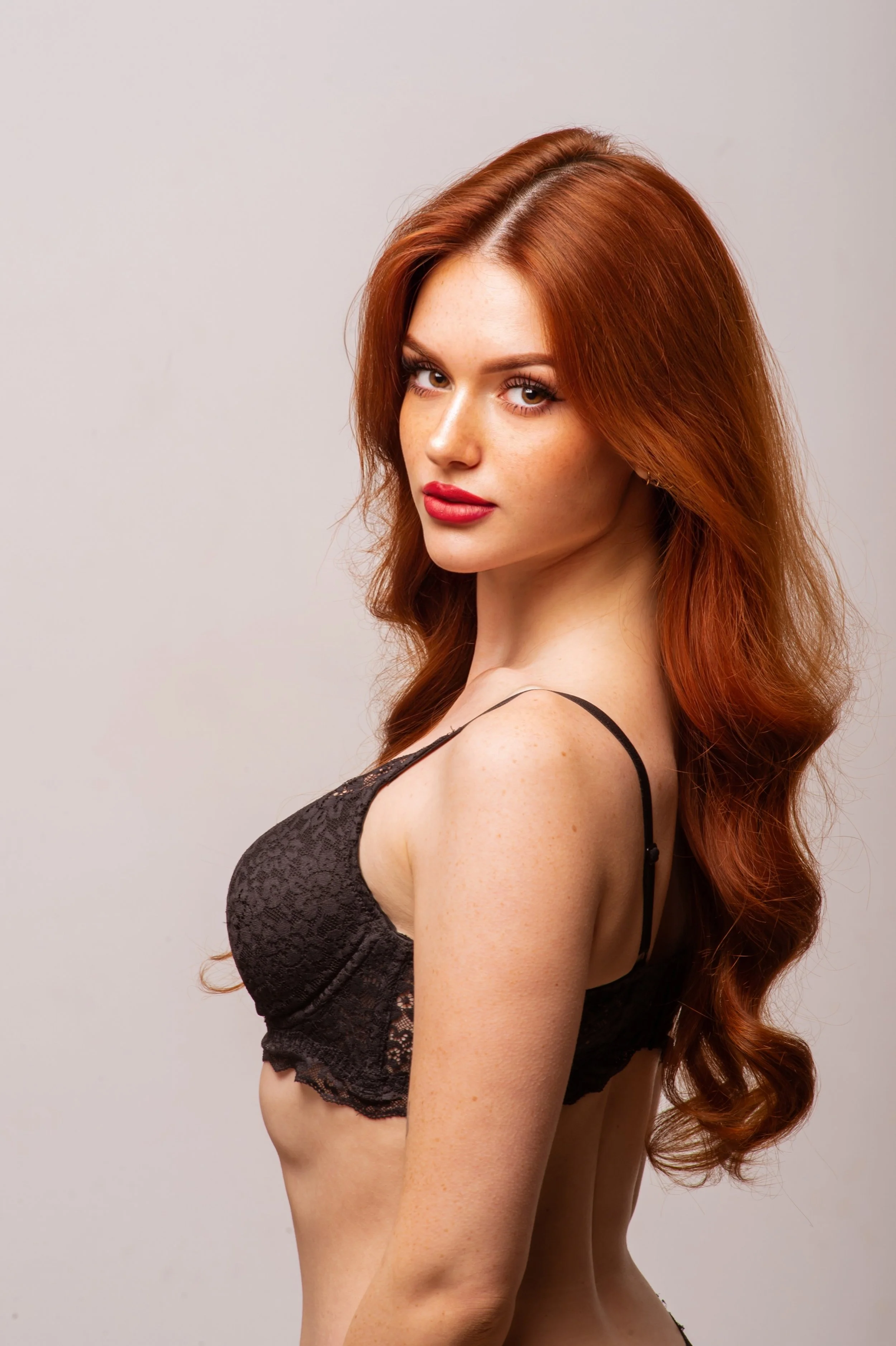 Ragazza con capelli rossi, indossa un top nero in pizzo, sfondo grigio chiaro.